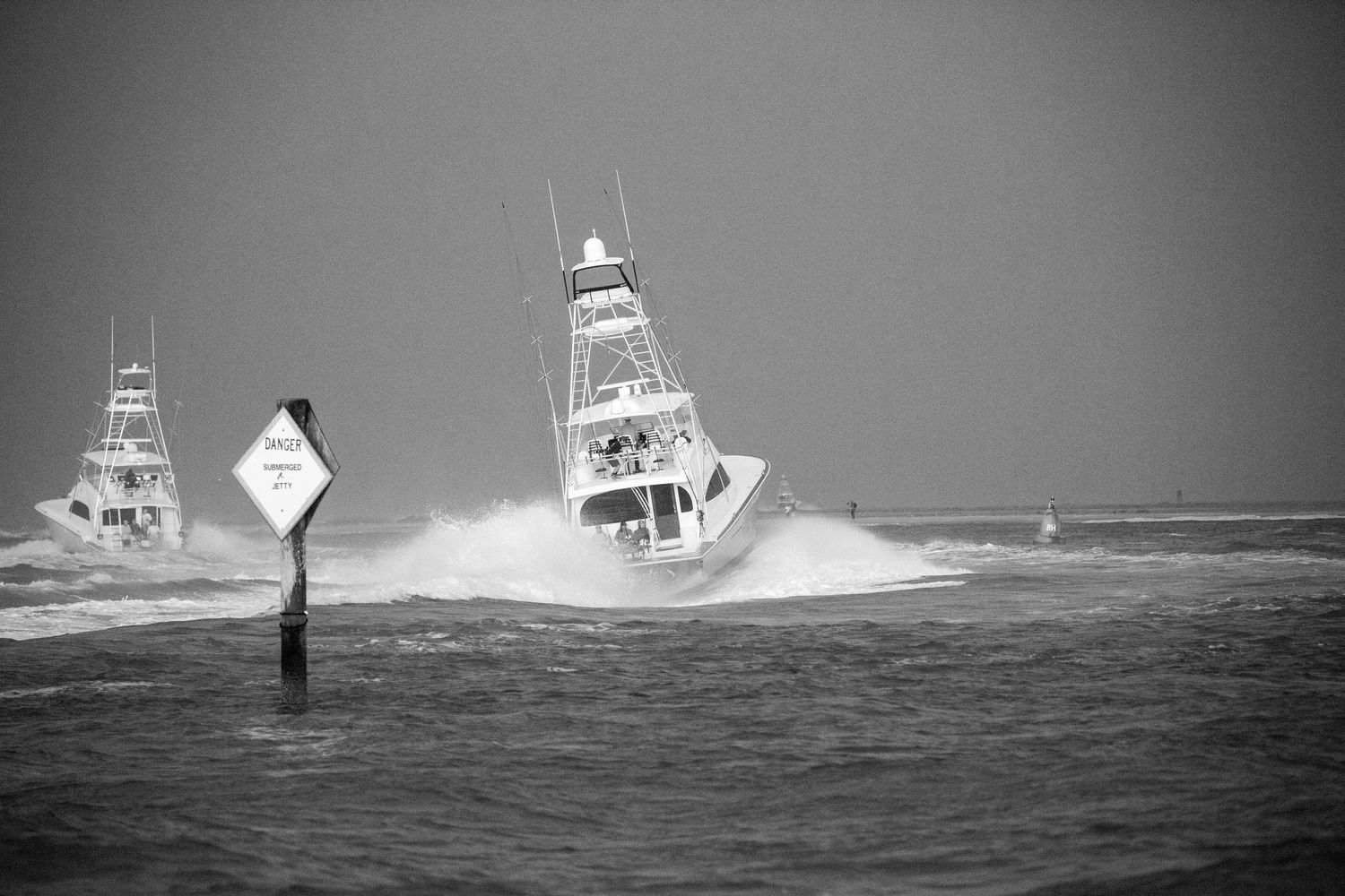 Sport fishing boats battle large waves while passing navigation markers in stormy seas.
