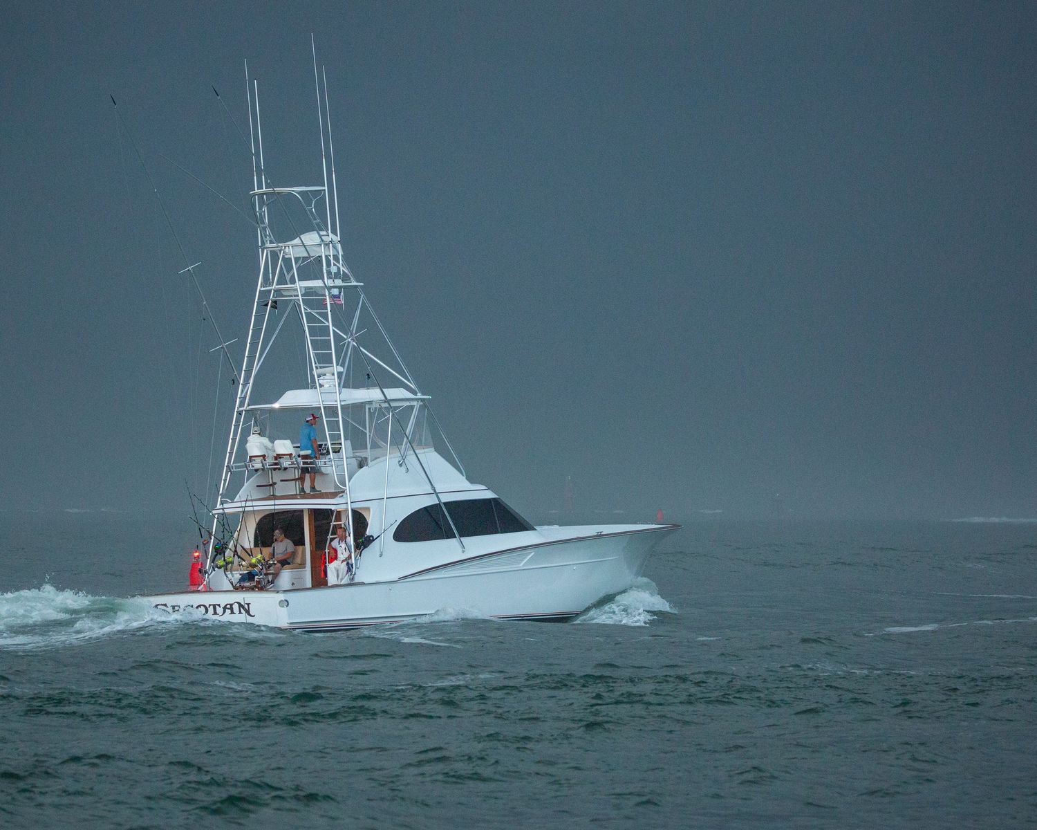 Sport fishing boat powering through stormy seas with dark clouds overhead.