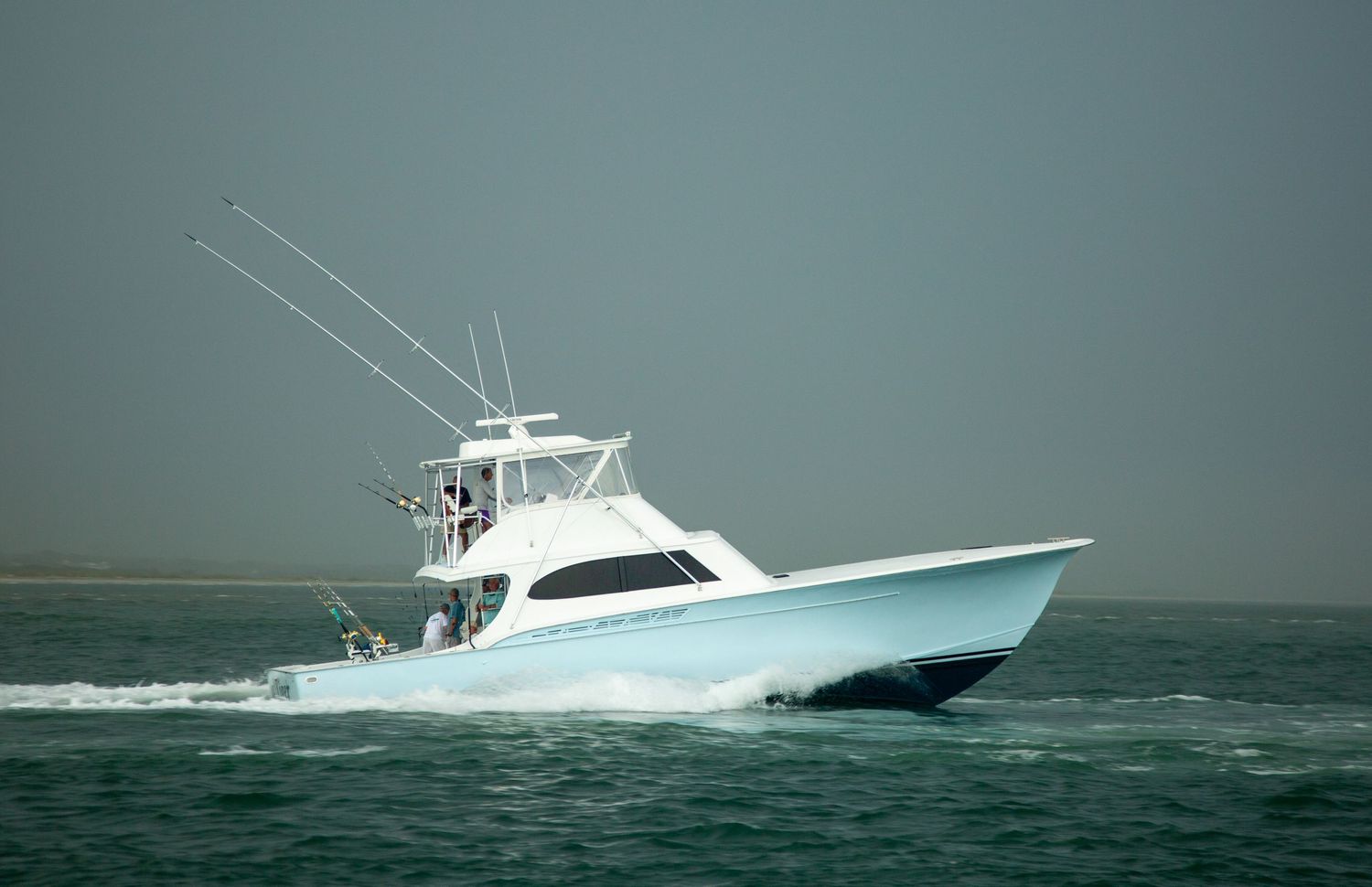 Large sport fishing boat slicing through choppy waters on an overcast day.