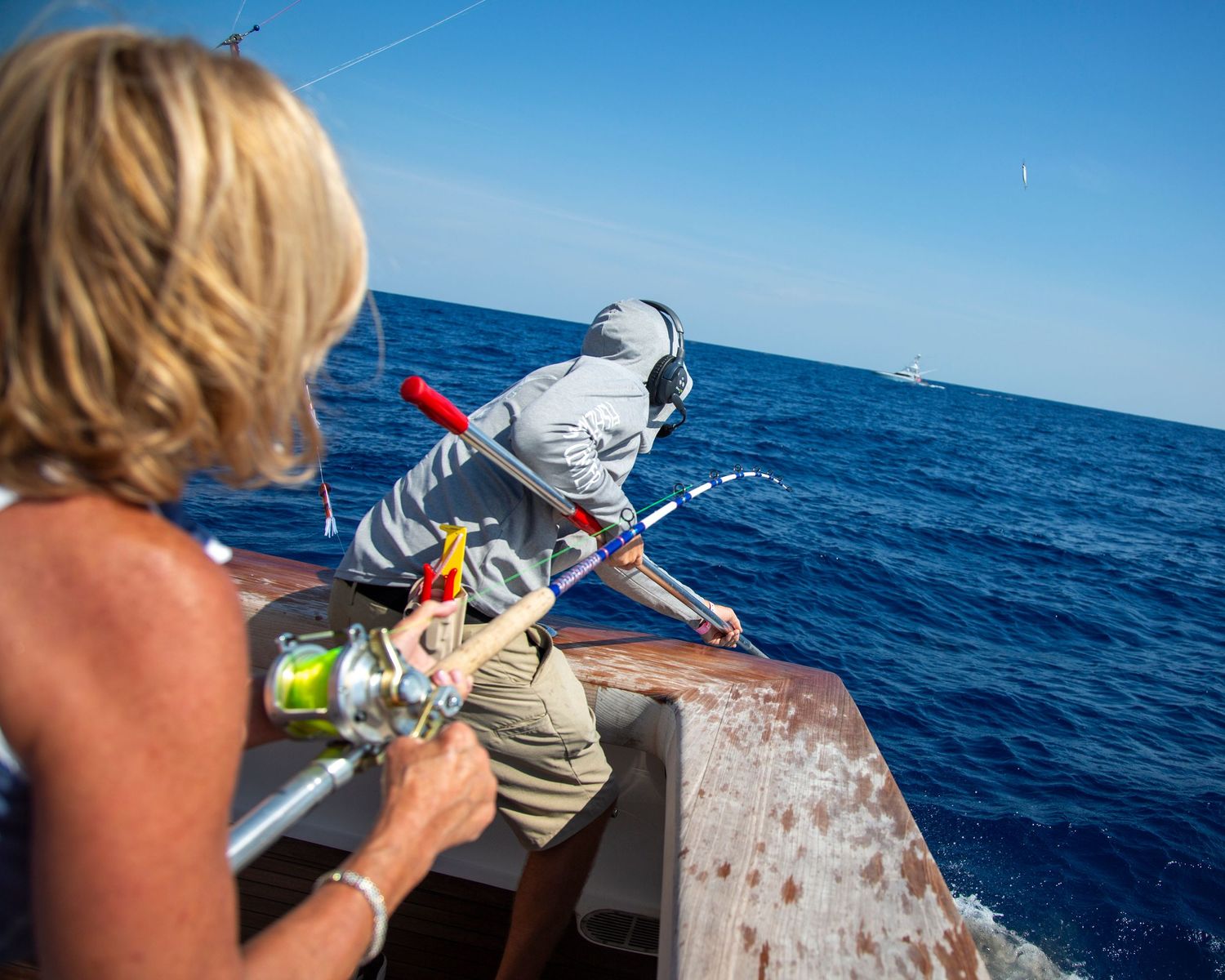 Two people fishing from a boat on the open blue ocean on a sunny day.