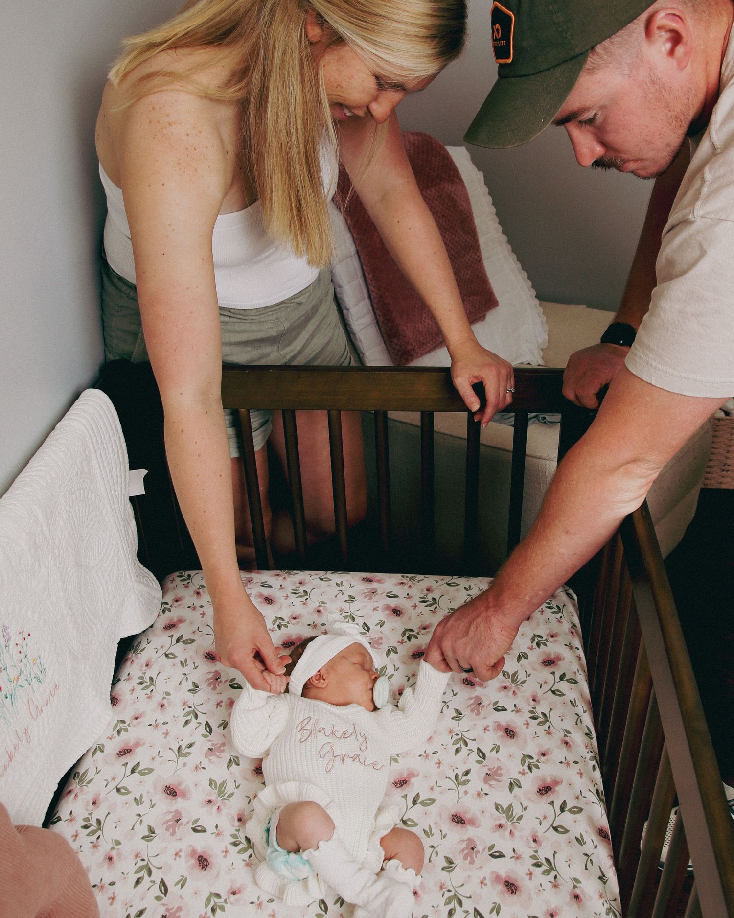Parents change an infant's diaper together on a floral patterned changing pad at home.