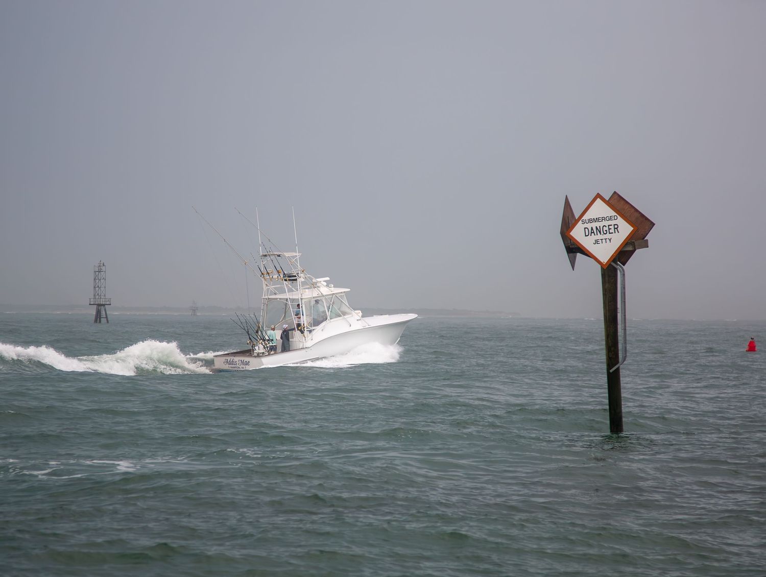 Sport fishing boat passing warning marker sign in rough coastal waters.