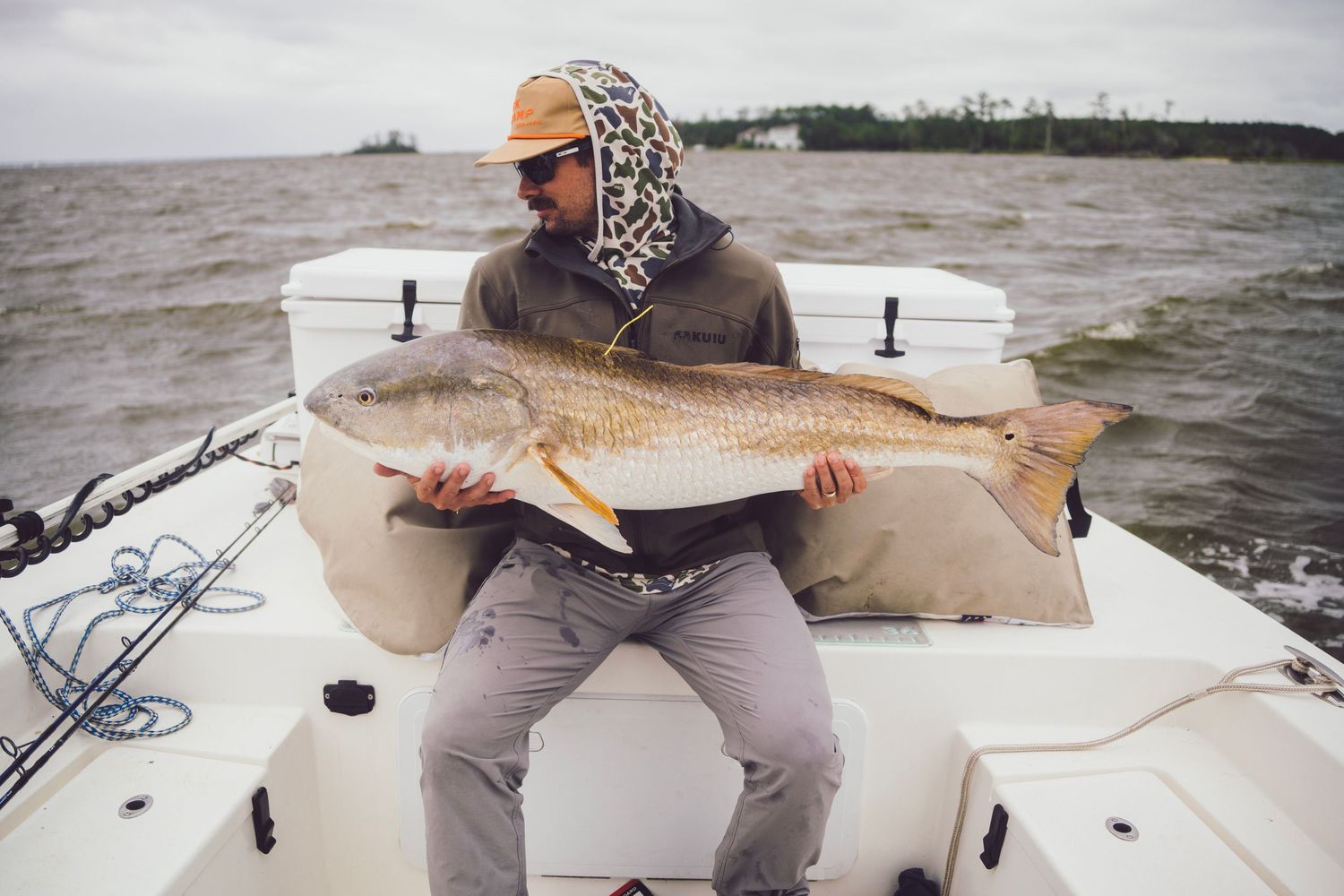 Angler sitting on a boat holding a large redfish catch on a cloudy day on open water.