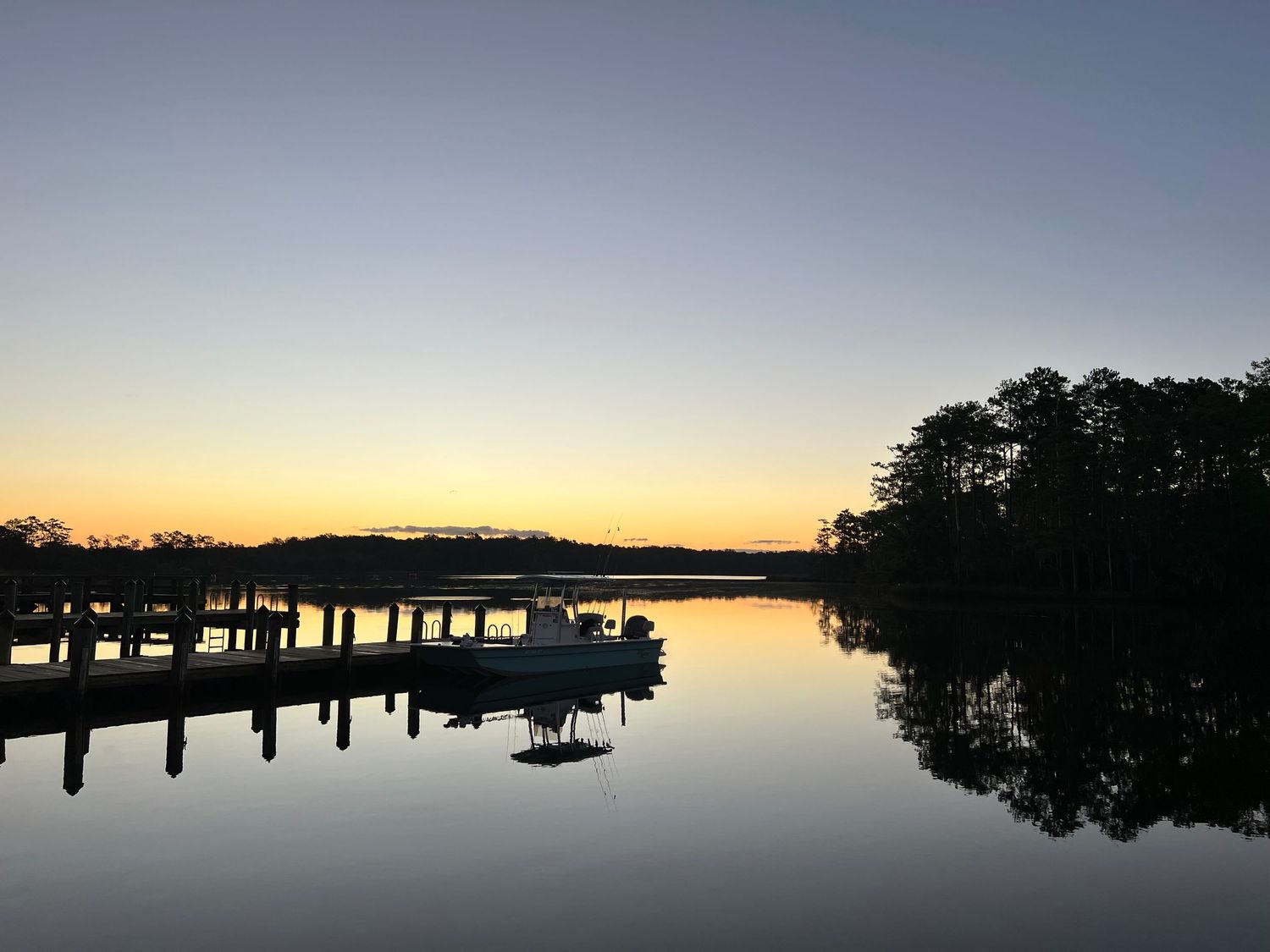 Silhouette of boats docked at a marina during sunrise prior to trip with calm water reflections and tree-lined shore.