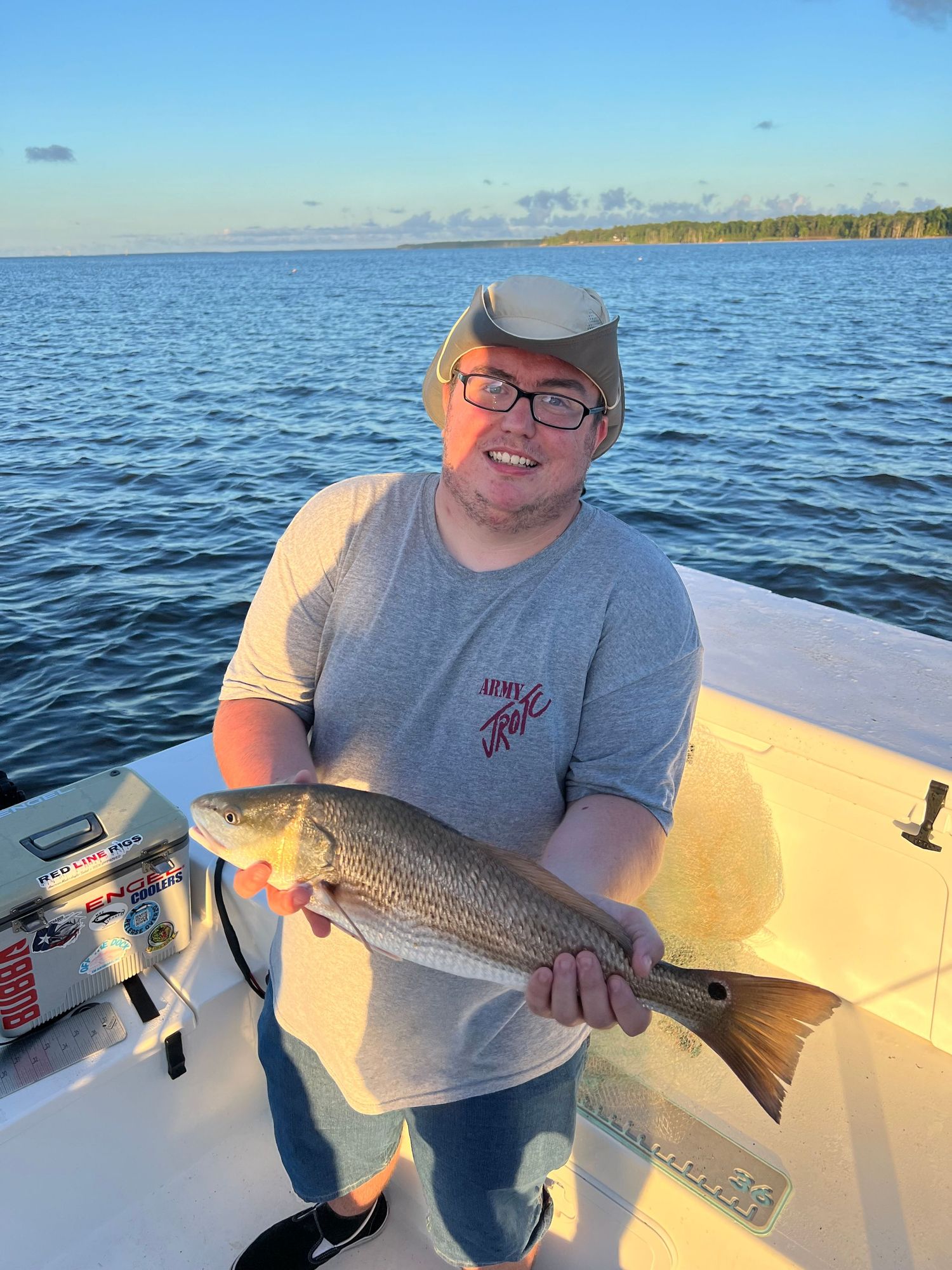 Happy angler shows off caught redfish from boat on sunny day over blue waters.