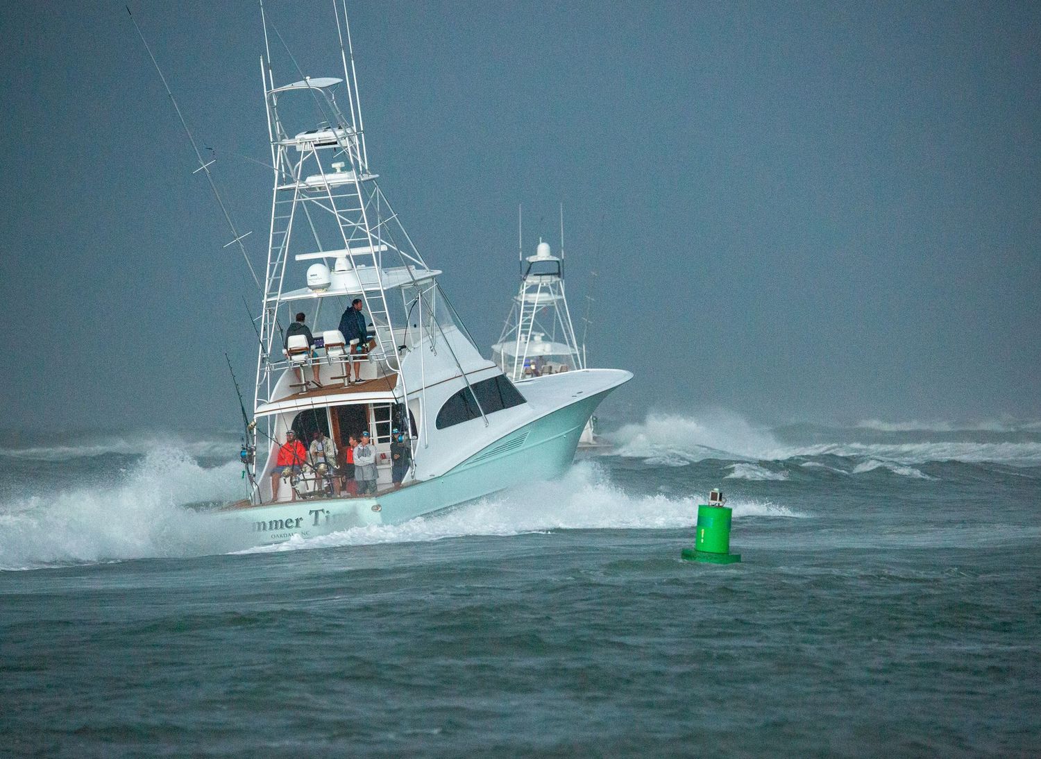 Charter boats navigate past channel markers in rough ocean conditions.