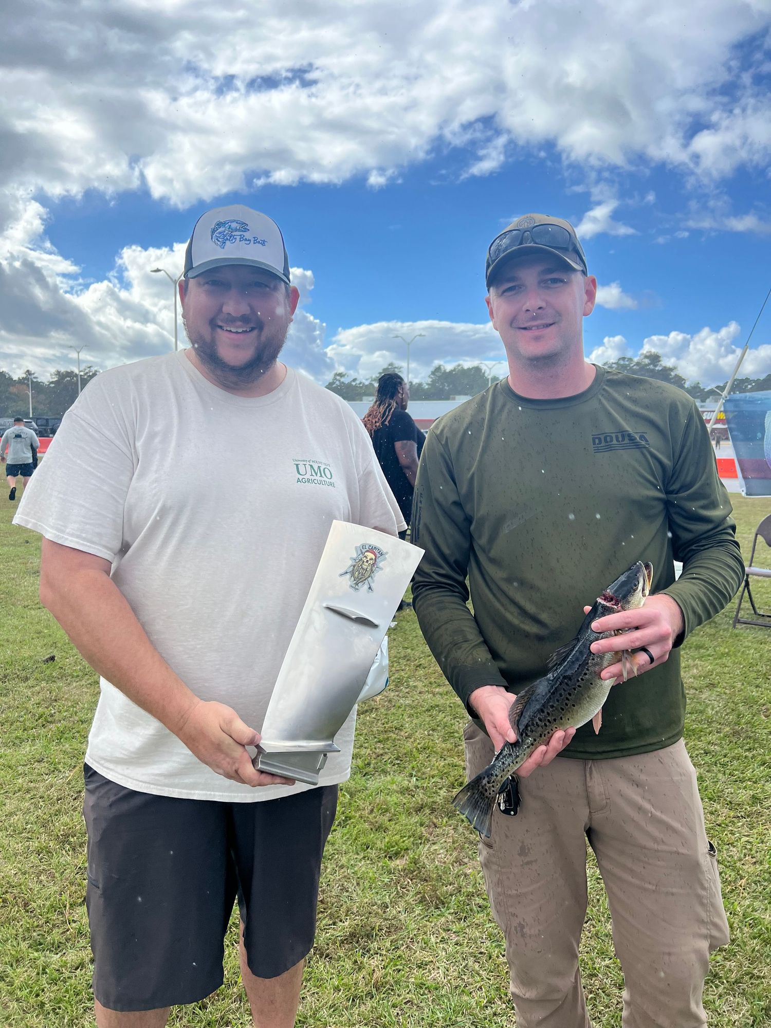 Two fishermen showing off their catches and equipment outdoors.