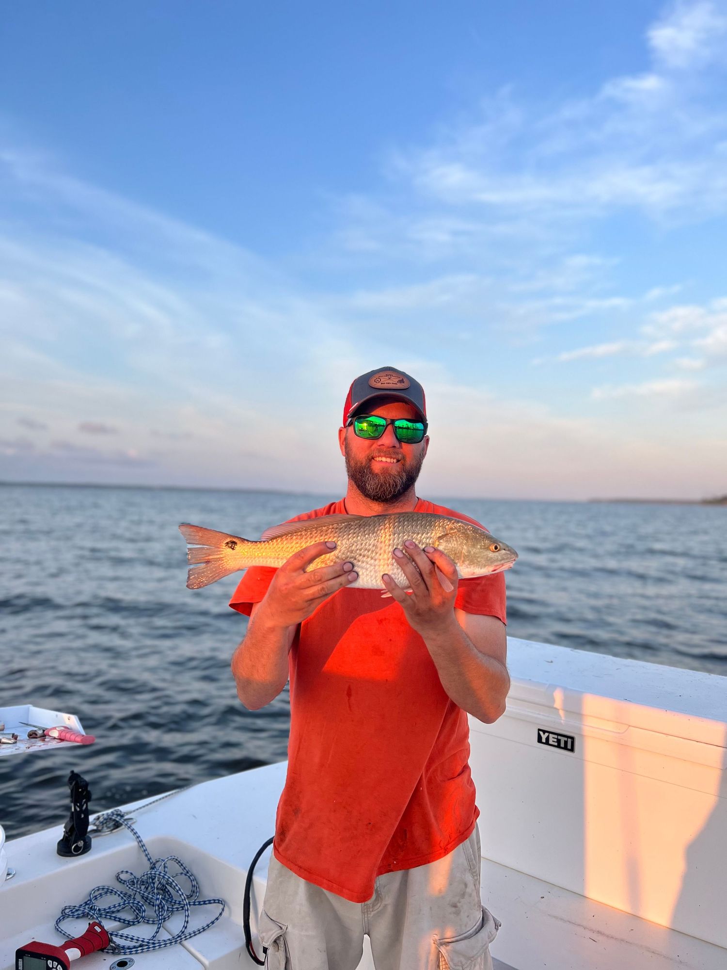 Redfish catch held up against vibrant sunset sky on white boat deck.