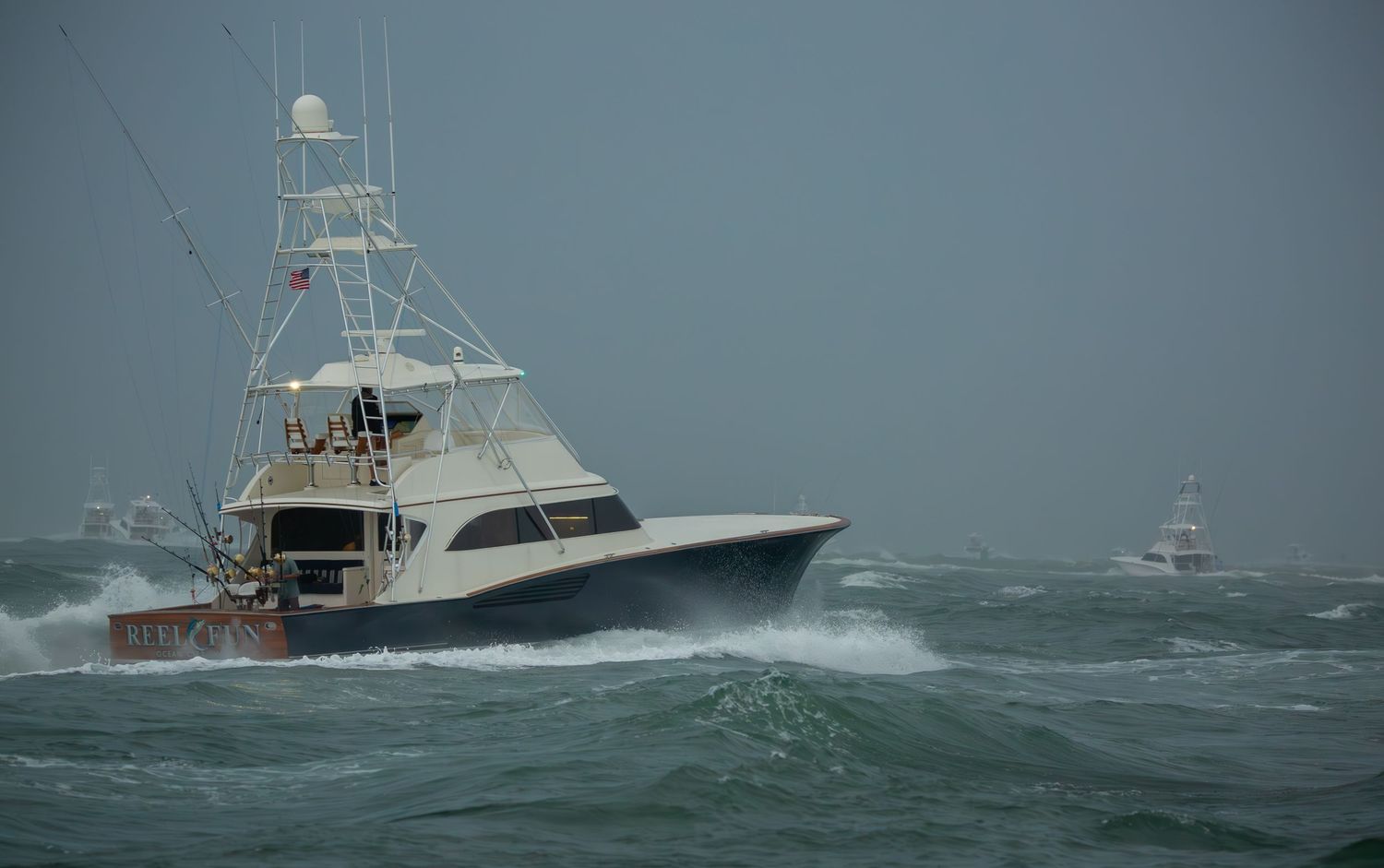 Fishing boats cutting through rough seas with white spray flying in gray weather.
