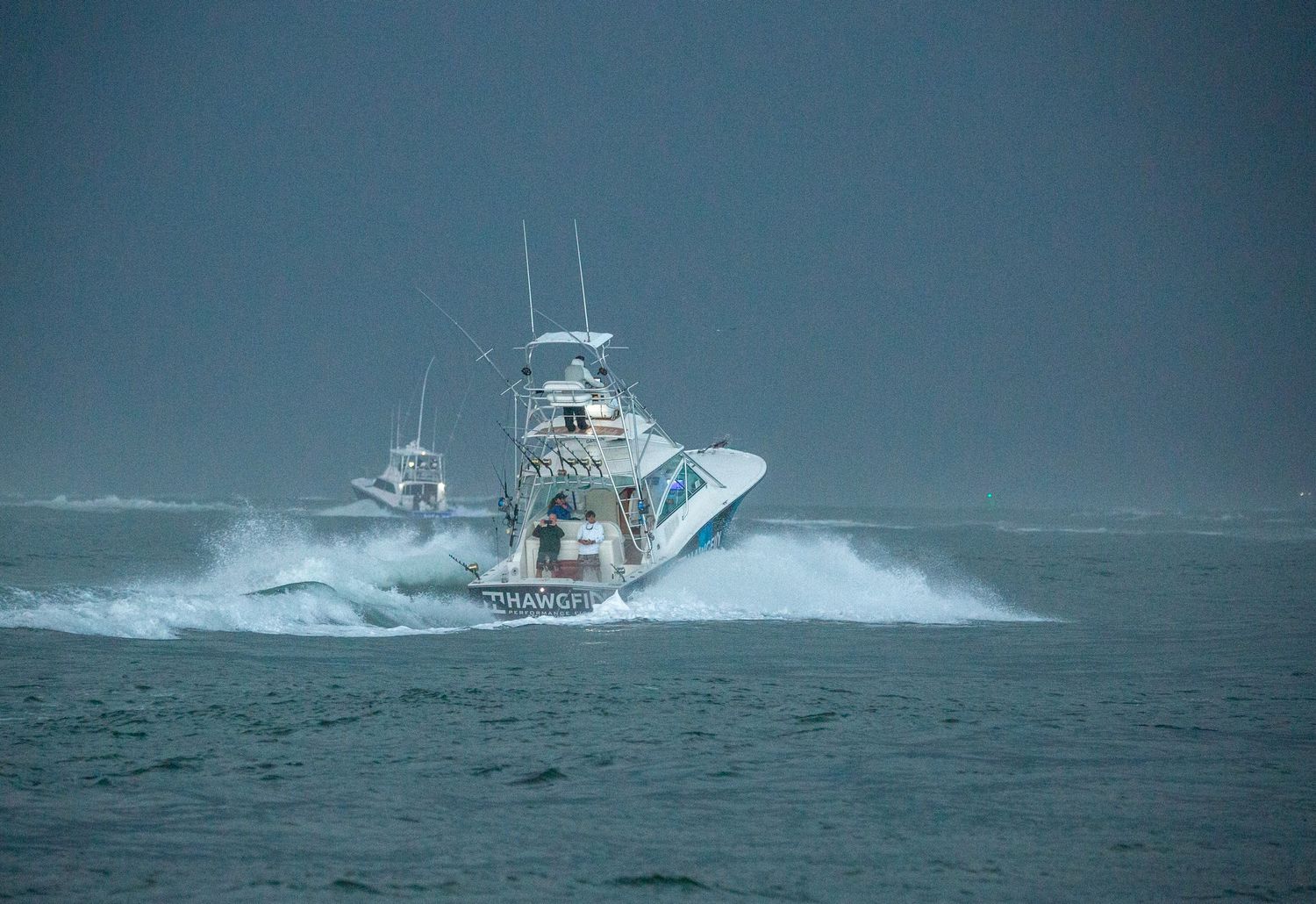 Fishing boats power through rough ocean waves in sequence.