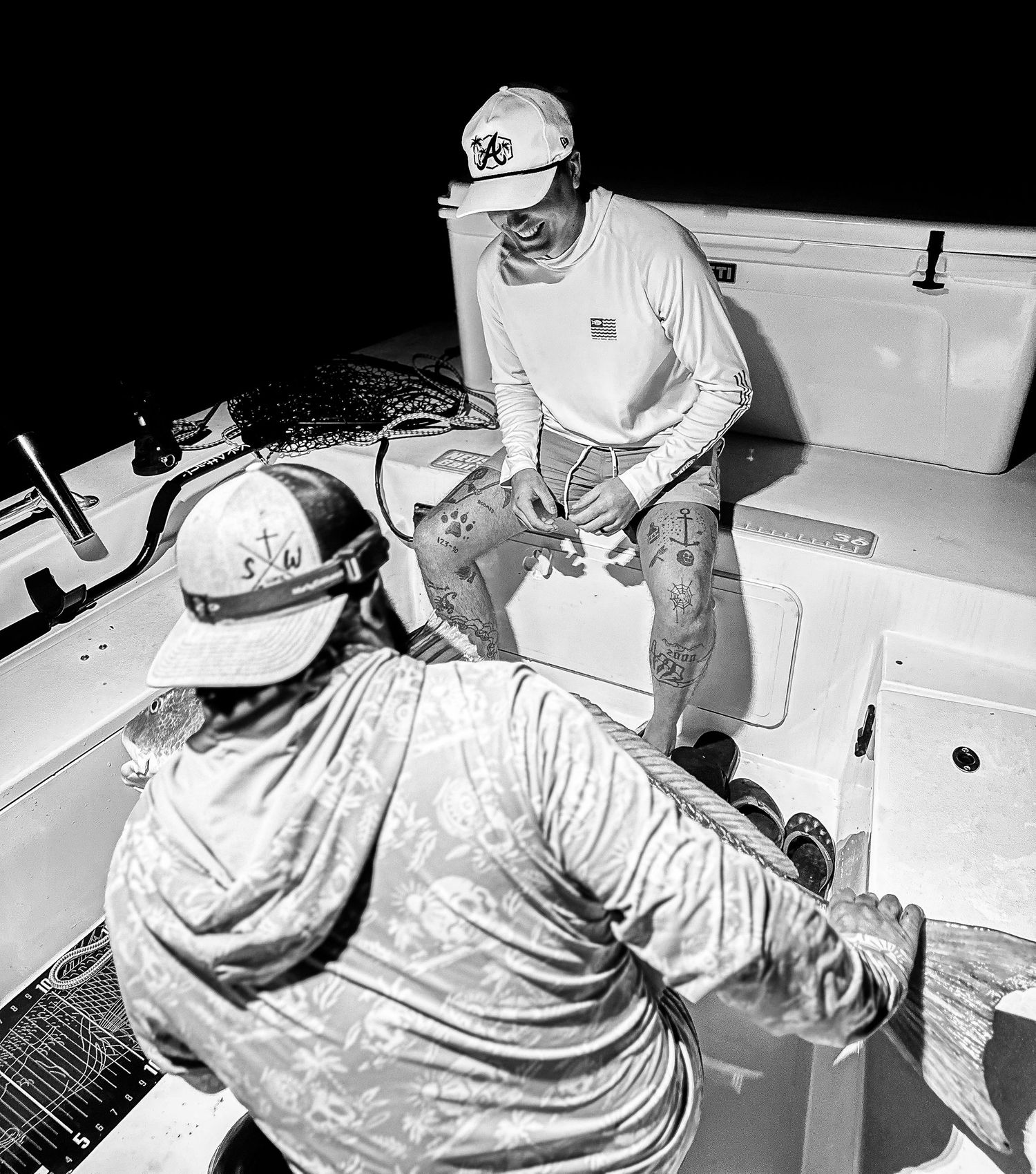 Two anglers on a boat at night holding a large spotted fish caught during a nighttime fishing trip.