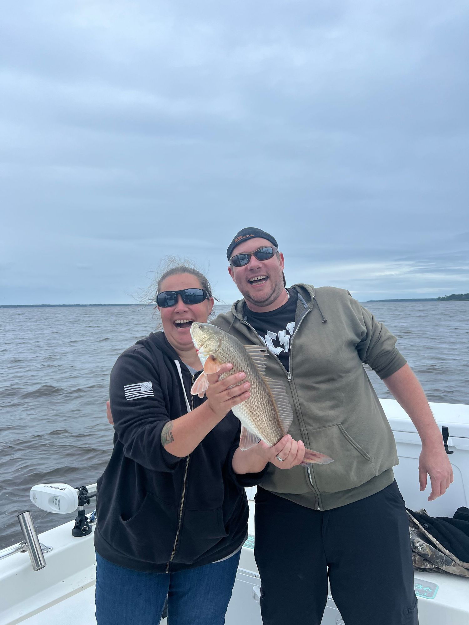 Anglers showing off their redfish catches while aboard a fishing boat on cloudy day.