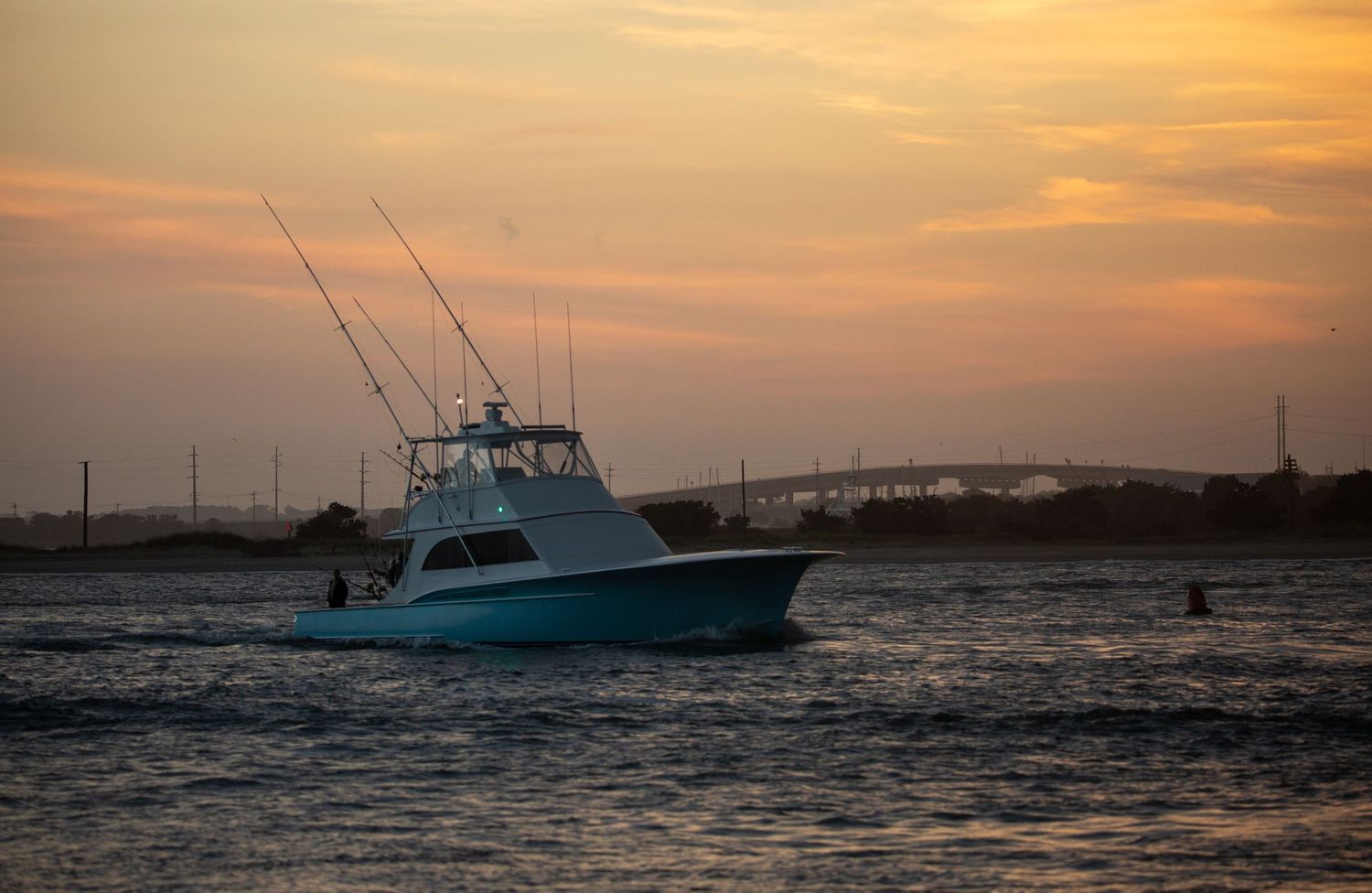 Silhouettes of fishing boats against an orange sunset on calm waters.
