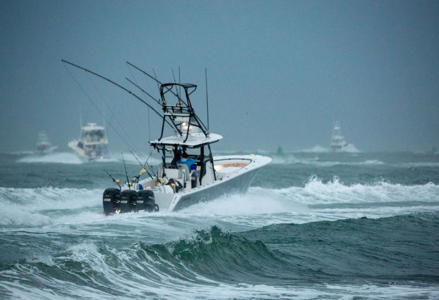 Sport fishing boat cuts through choppy blue waters on a cloudy day.