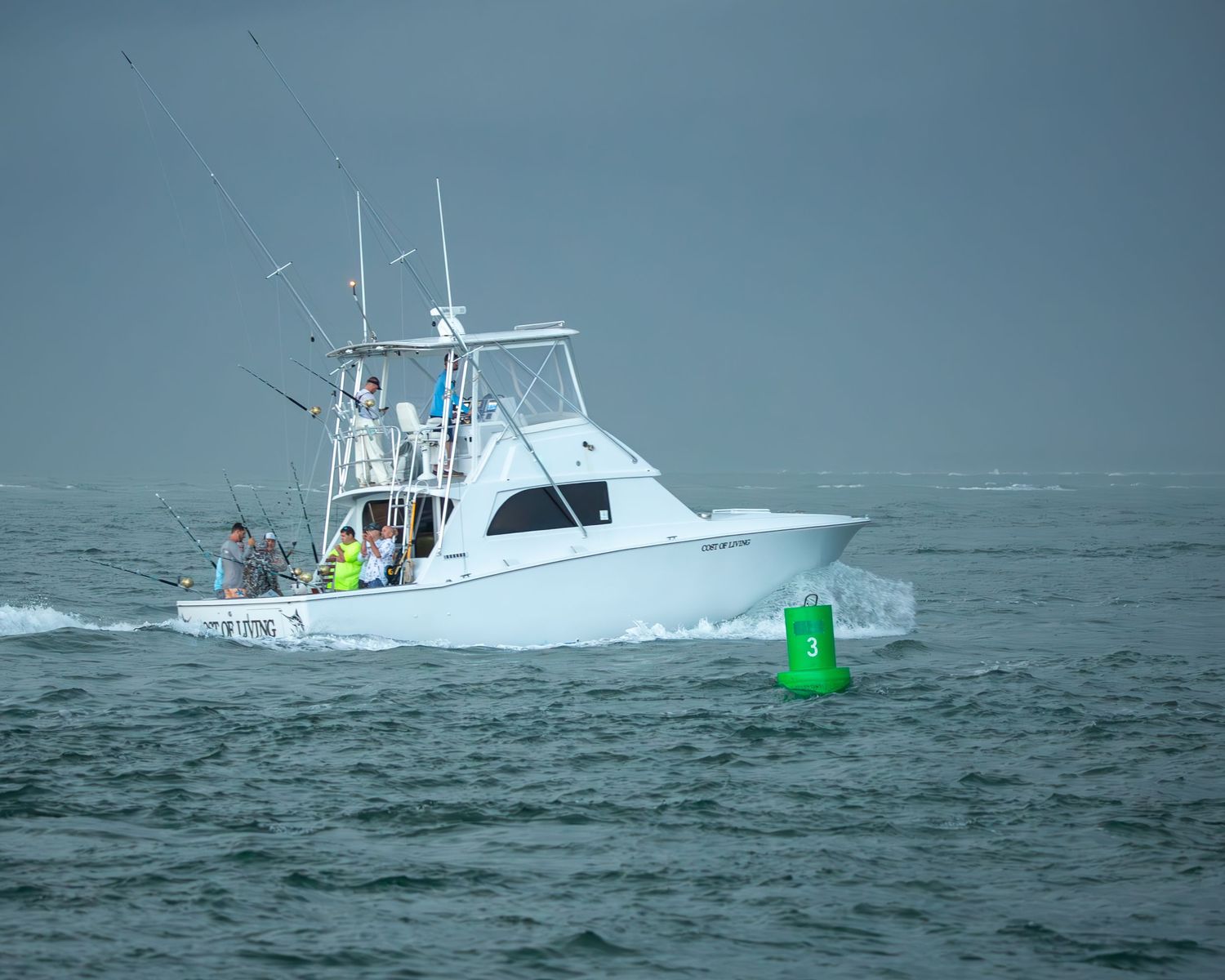 White sport fishing boat passes a green channel marker in rough ocean conditions.