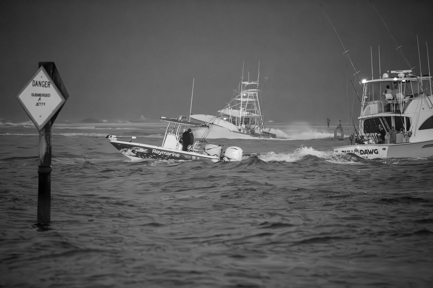 Sport fishing boats navigate rough seas past channel markers in black and white stormy conditions.