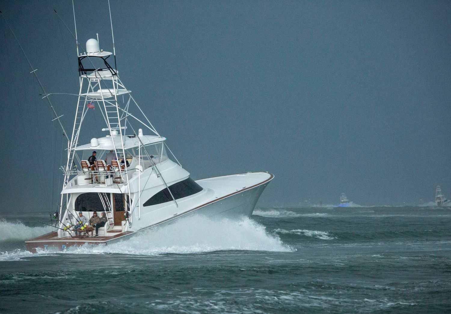 Sport fishing vessels power through rough ocean swells near coastal markers.