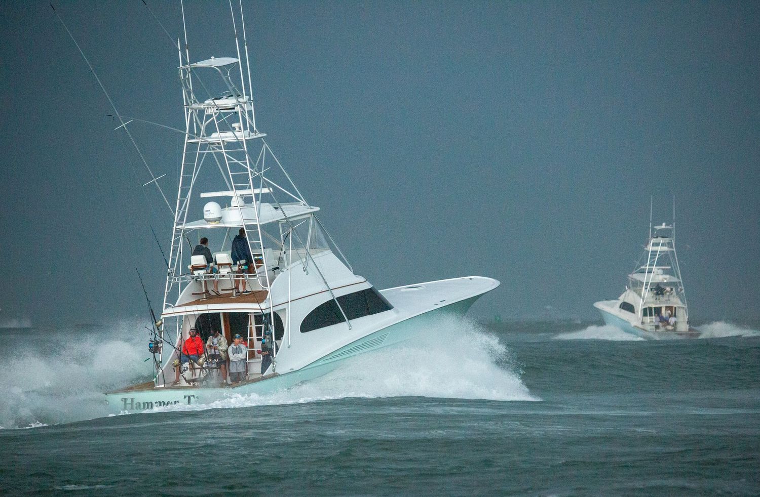 Multiple fishing boats traverse through stormy waters with high swells.