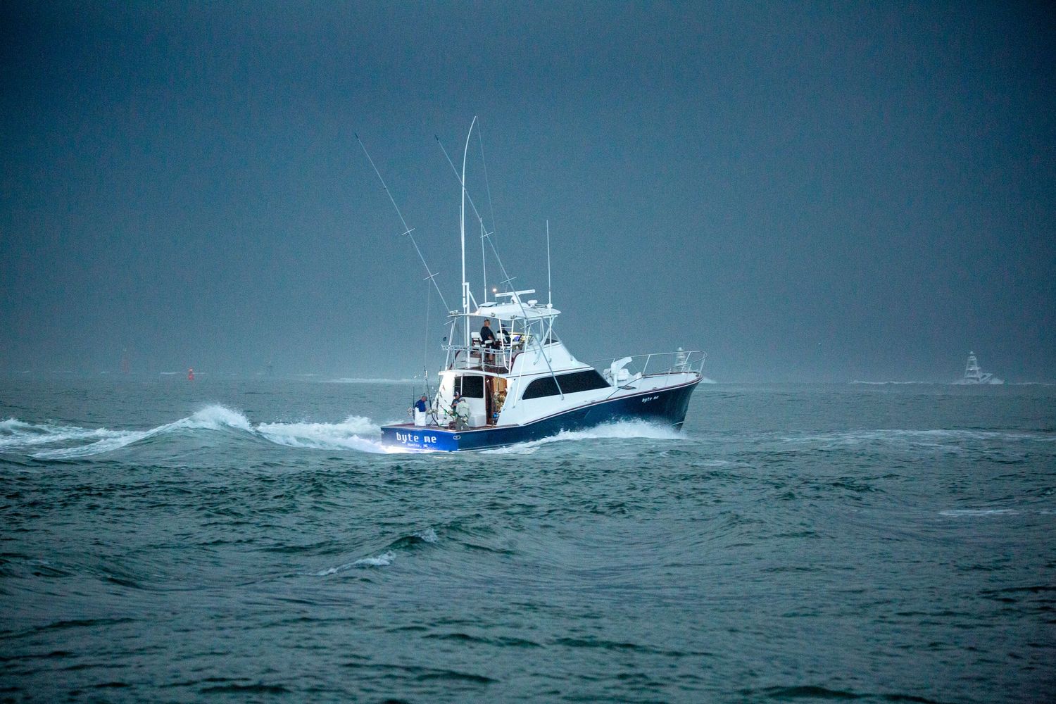 Sport fishing vessel powers through choppy seas with blue hull visible in rough conditions.