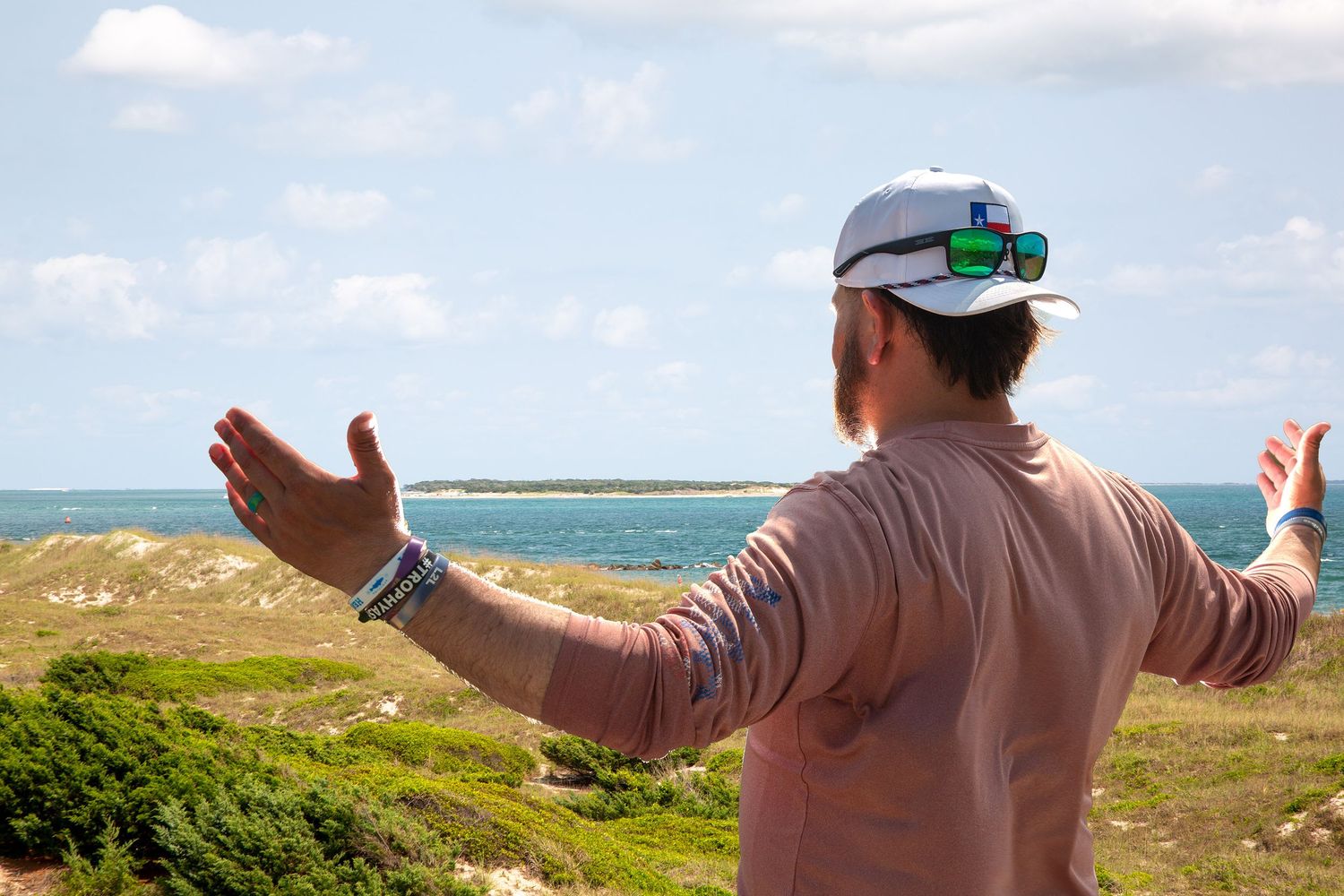 Person with outstretched arms enjoying scenic coastal views on a sunny day.