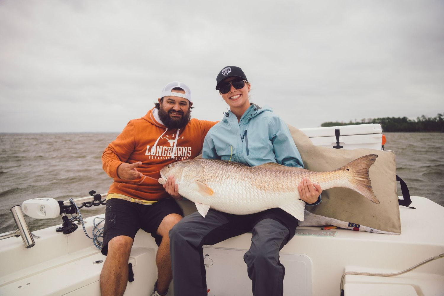 Two anglers proudly display a large redfish caught on a boat during a cloudy day on the water.