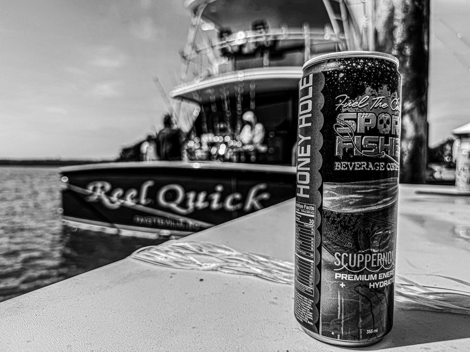 Black and white photo of a Scupper Pro energy drink can on a boat named Reel Quick docked at a marina.