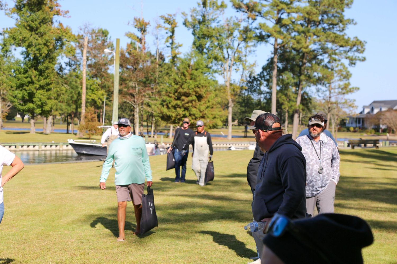 Fishing tournament participants and officials gathered on grassy area near boats.