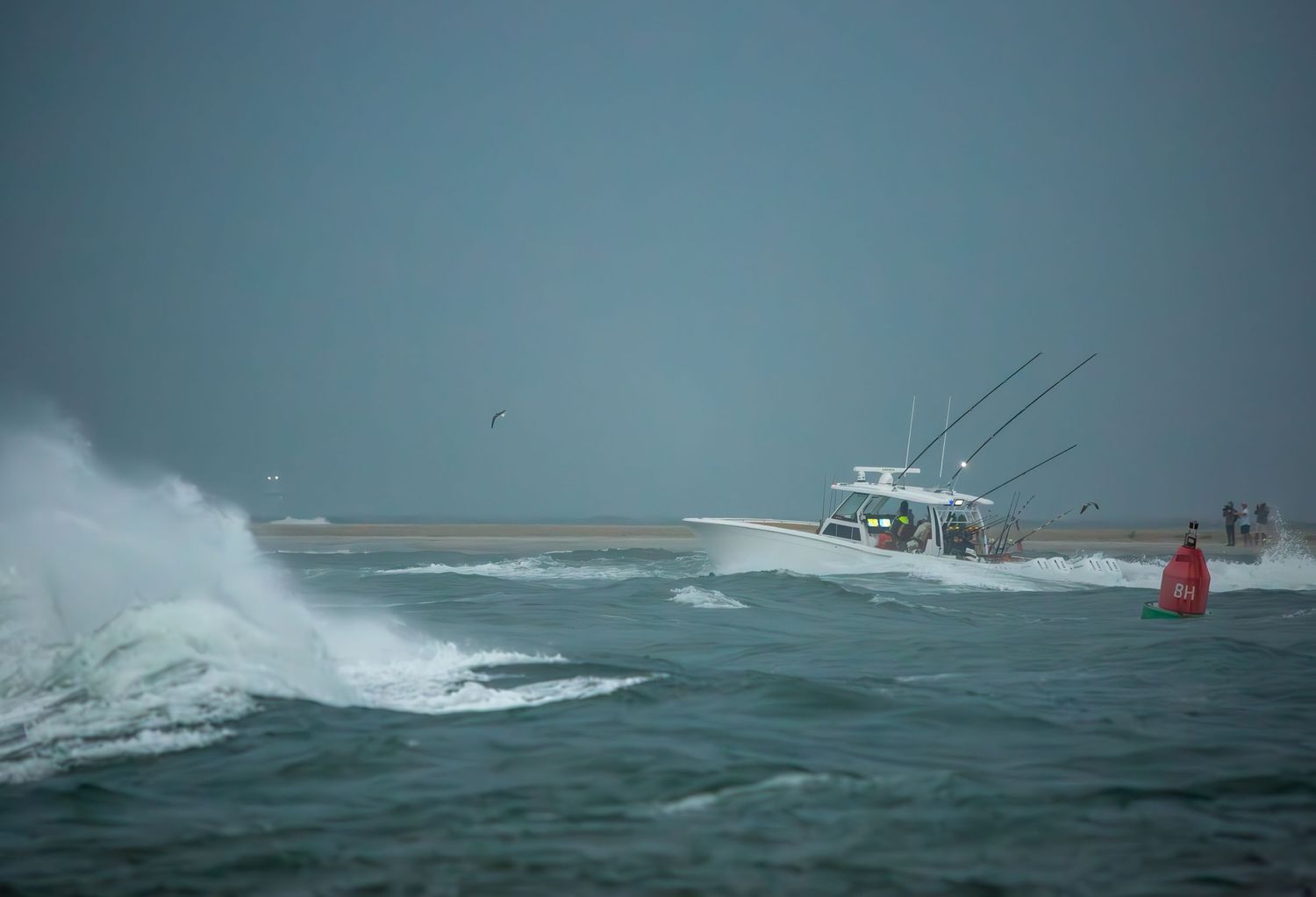 White sport fishing boat powers through large ocean swells near shore.