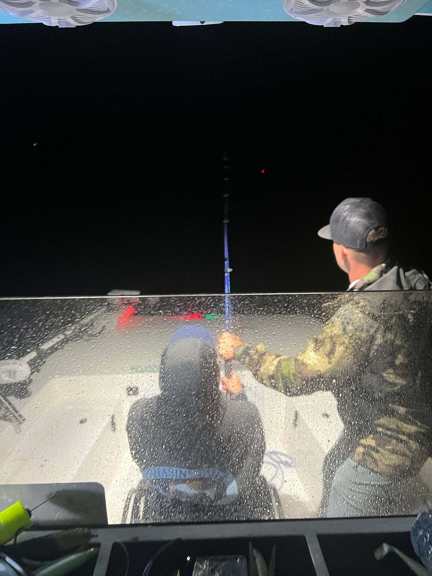 Night fishing scene showing anglers illuminated by boat lights on dark water.