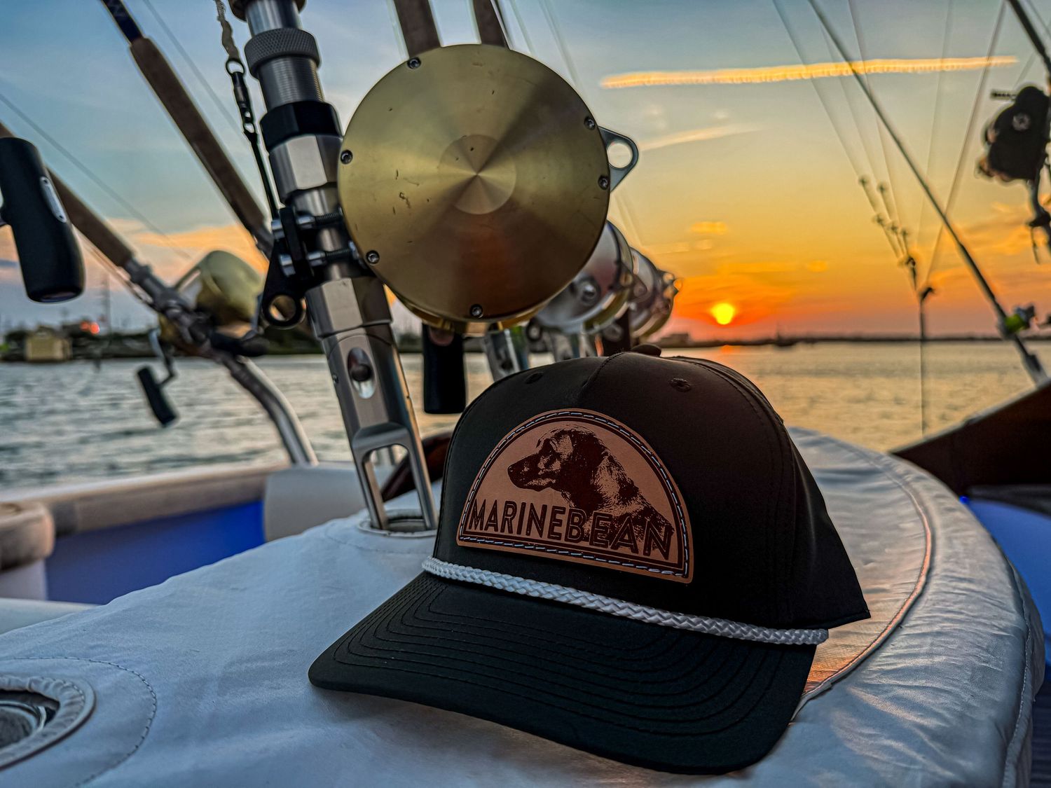 Marine Boat trucker hat displayed on a fishing boat deck against a stunning golden sunset over the water.