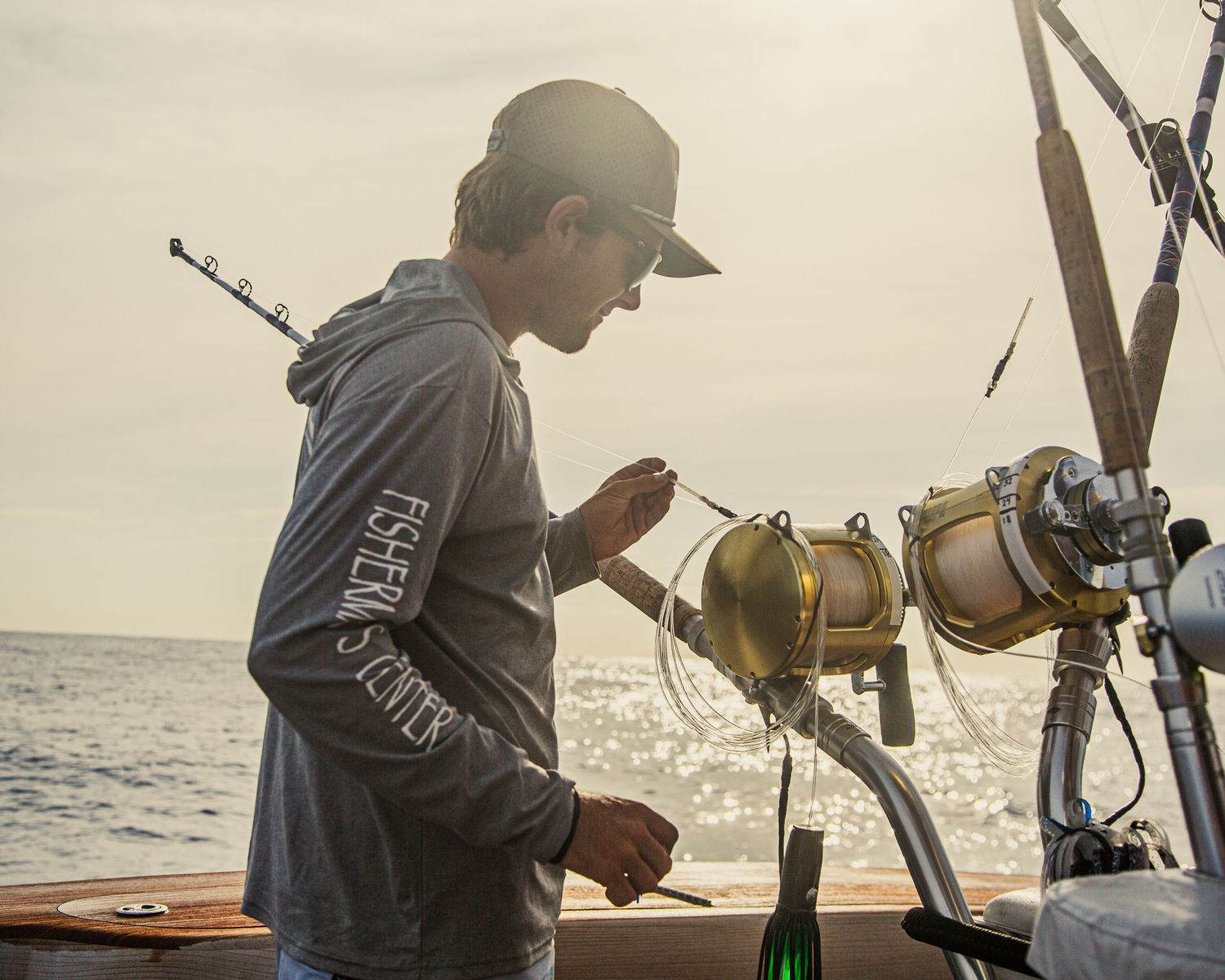 Angler in fishing shirt adjusting tackle on sport fishing boat at golden hour sunset.