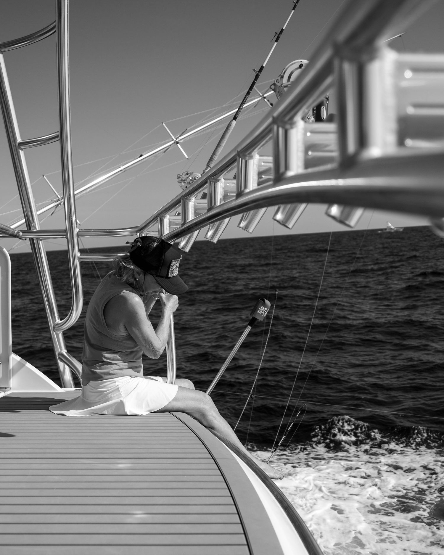 Woman sitting on the deck of a sailboat at sea, captured in black and white photography.