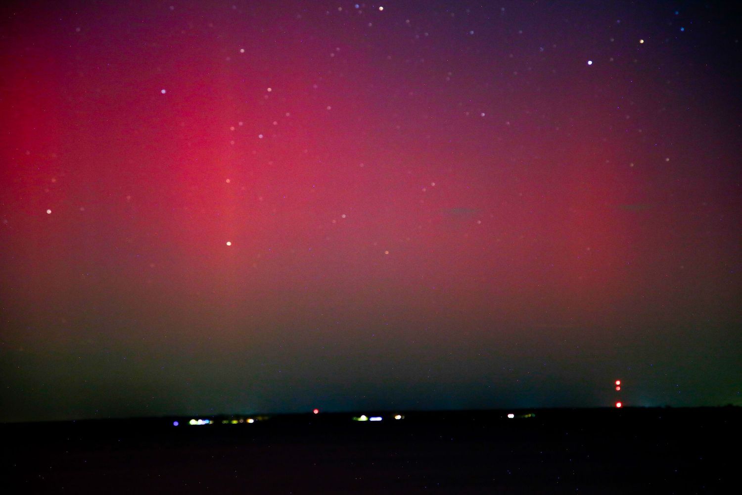 Stunning aurora borealis display with vibrant red and green lights illuminating the night sky over a dark horizon.