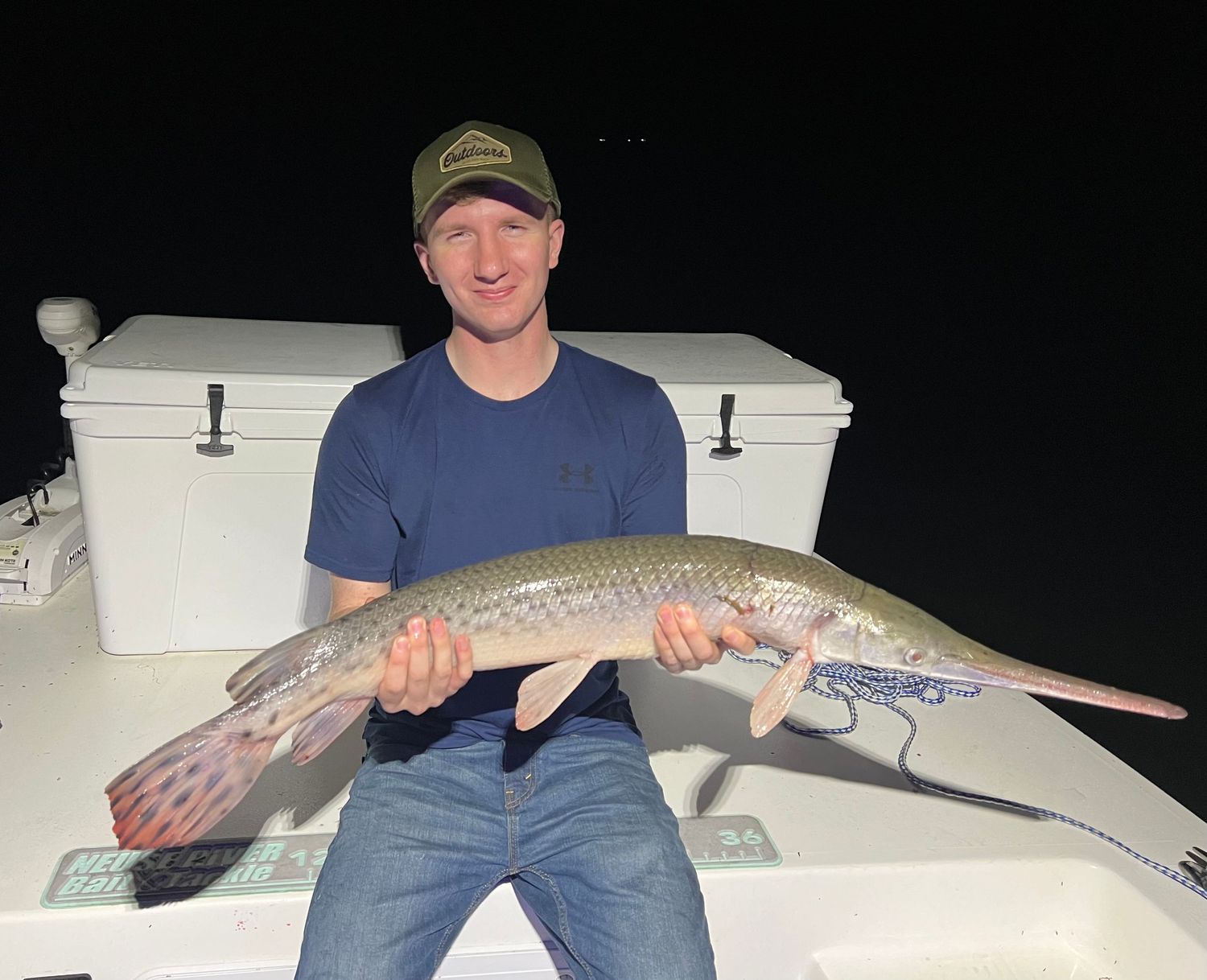 Large fish catch displayed against white coolers on boat deck at night.