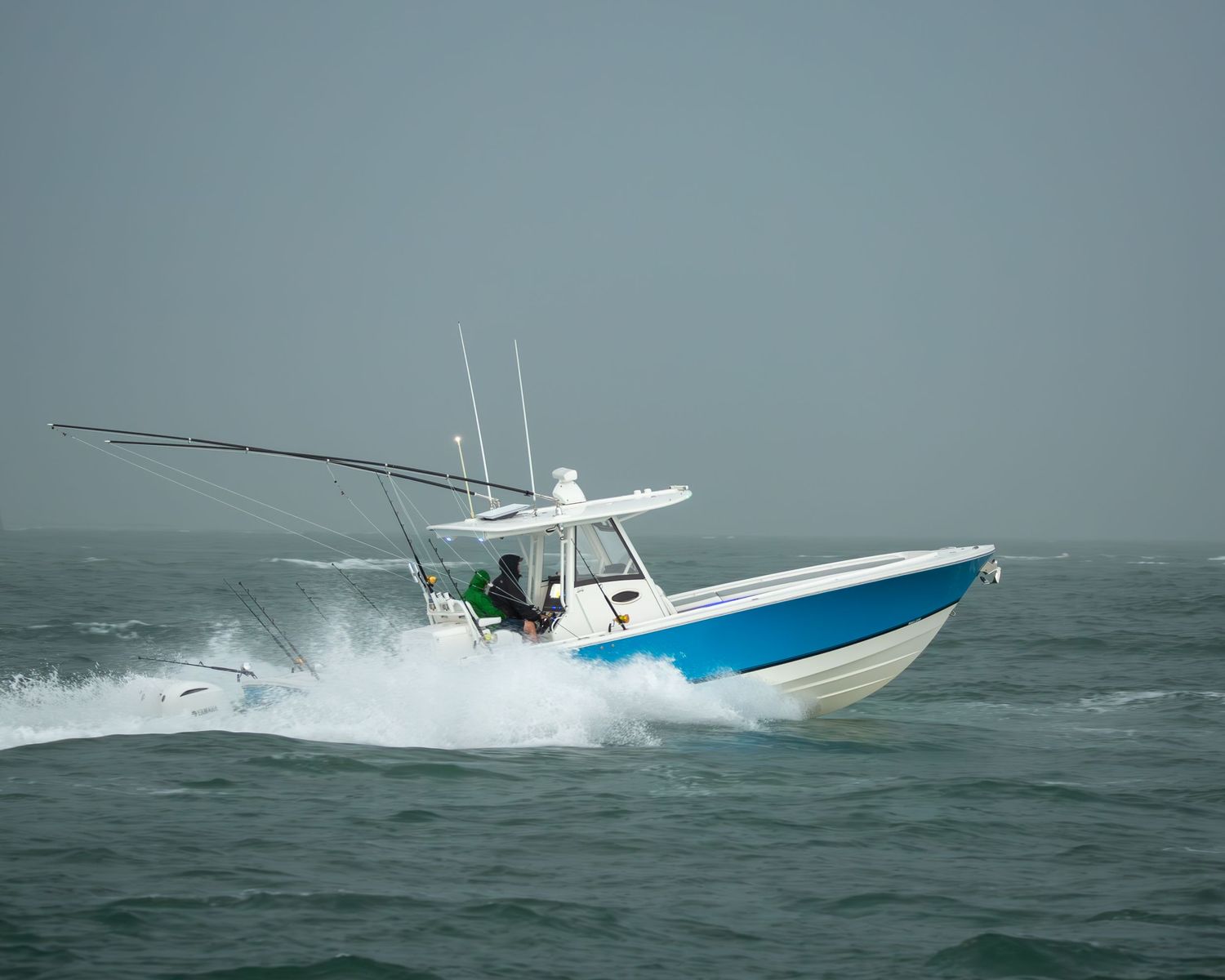 A blue and white center console fishing boat powers through rough seas with fishing rods deployed.