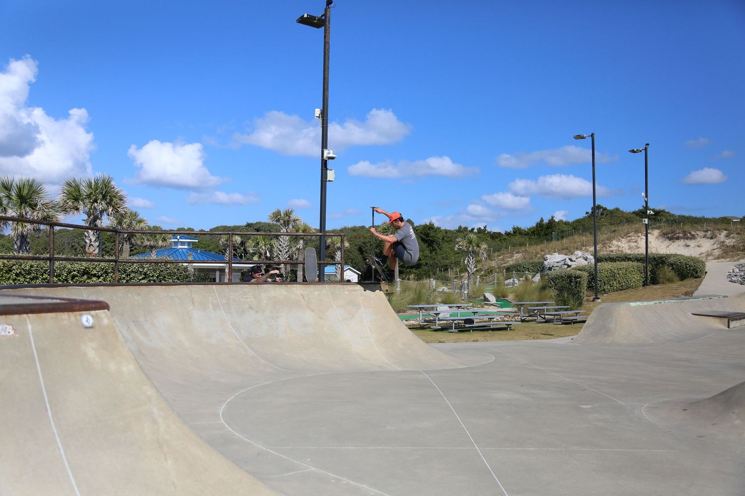 Wide panoramic view of a skate park ramps and features under blue sky with white clouds.