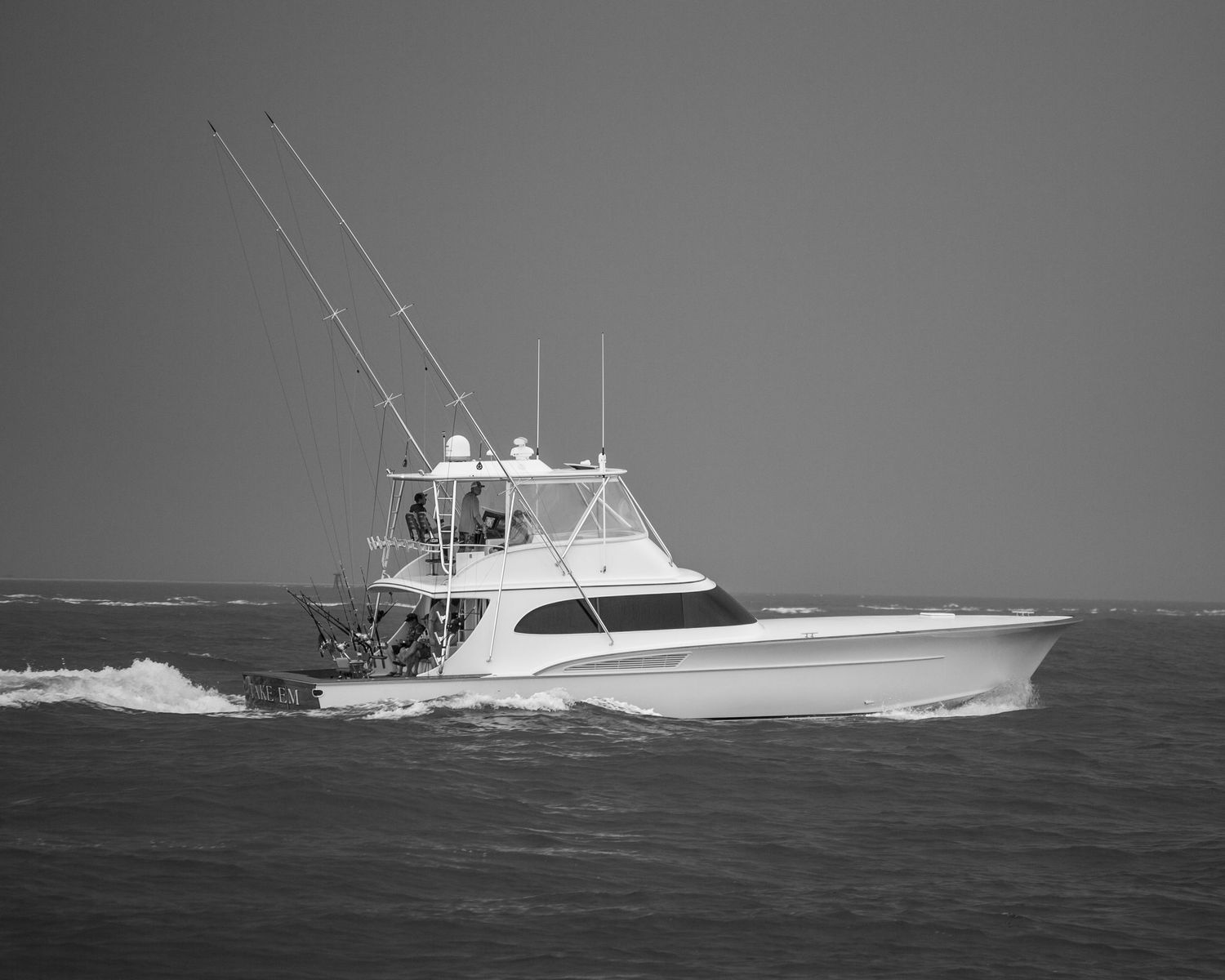 Black and white photo of a luxury sport fishing yacht cruising on open water with fishing outriggers extended.