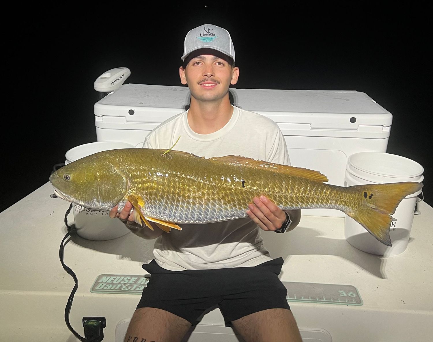 Large redfish catch displayed on a boat deck at night.