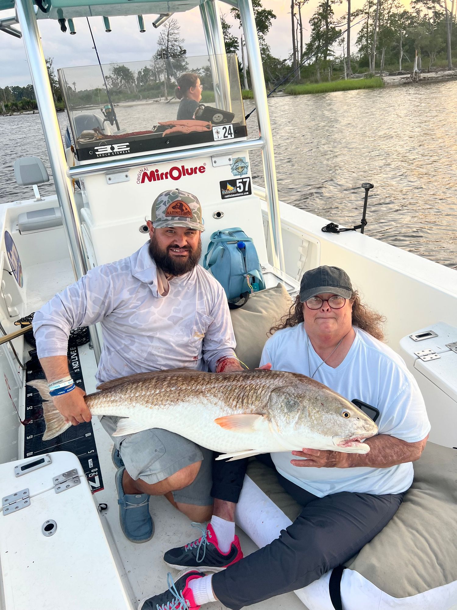 Several anglers displaying their redfish catches aboard a white fishing vessel.