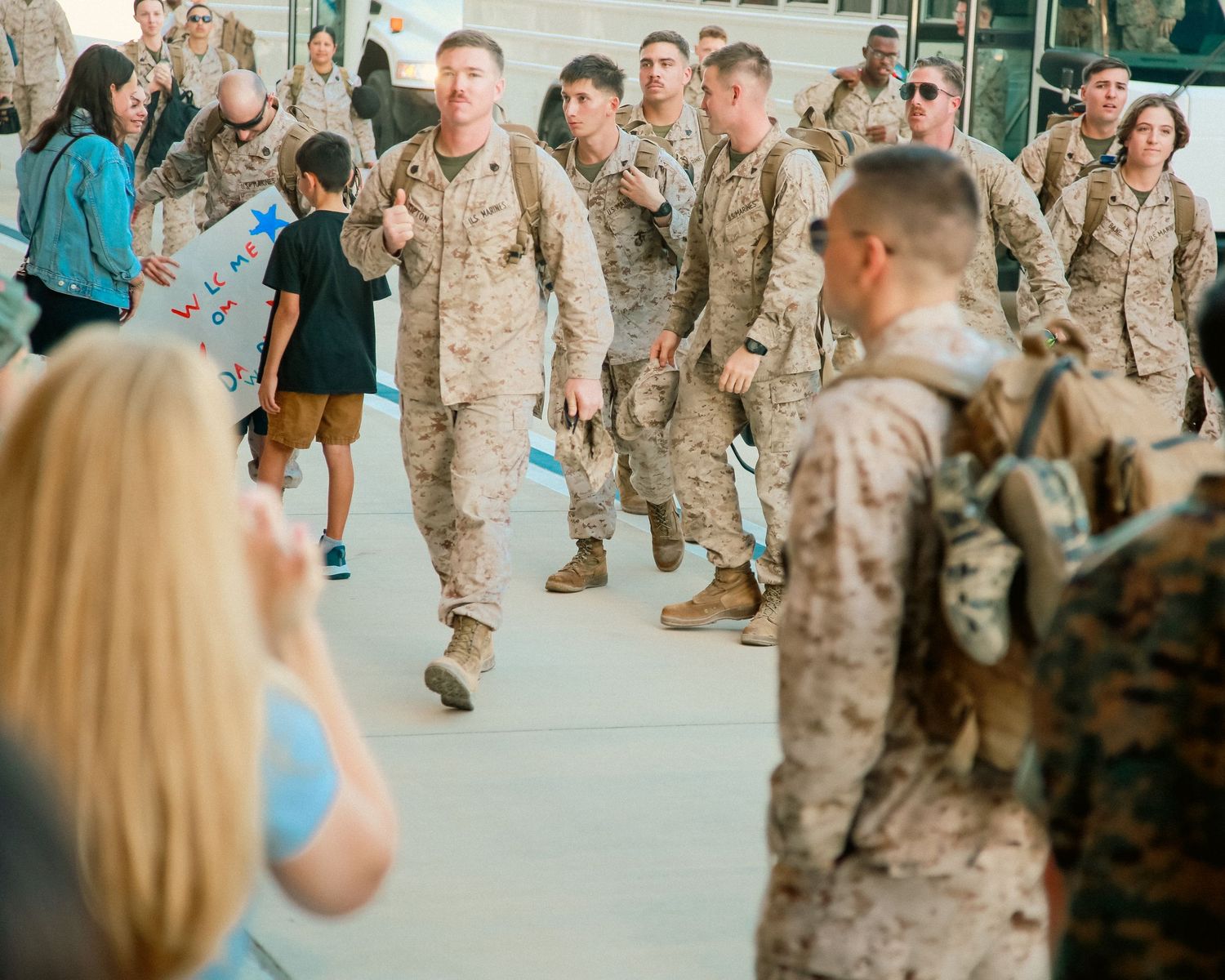 Military service members in desert camouflage uniforms gather in a large indoor space.