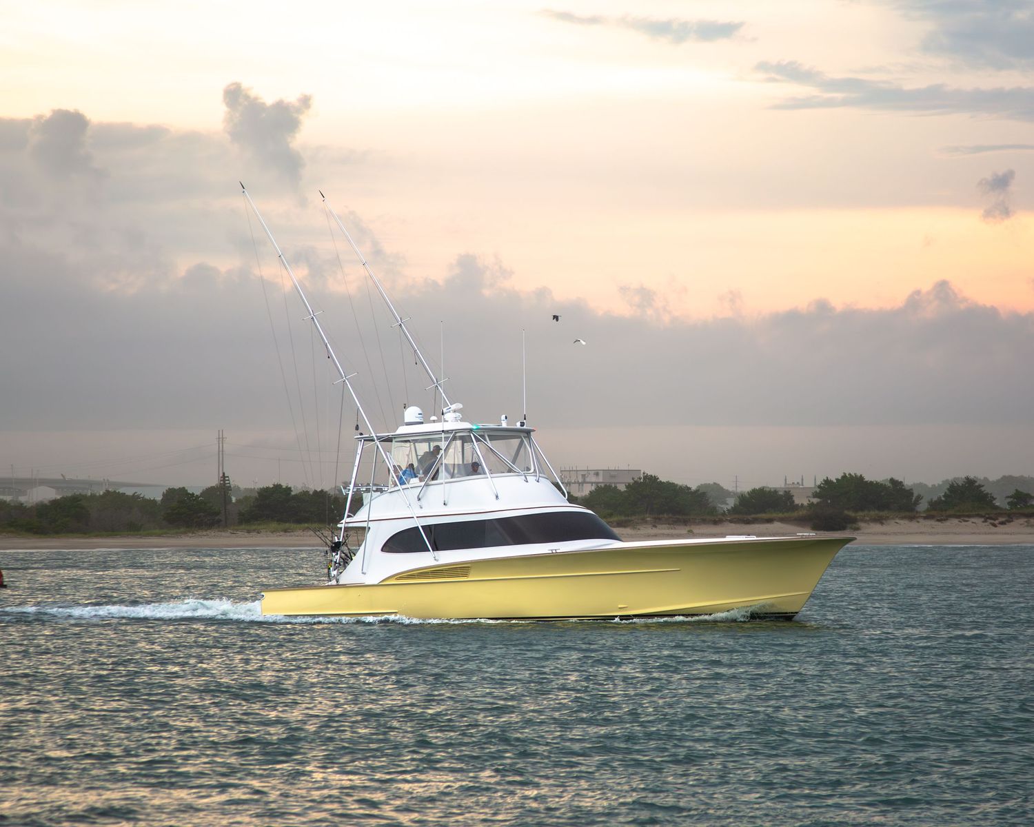Yellow and white sport fishing yacht cruises at sunset in calm coastal waters.