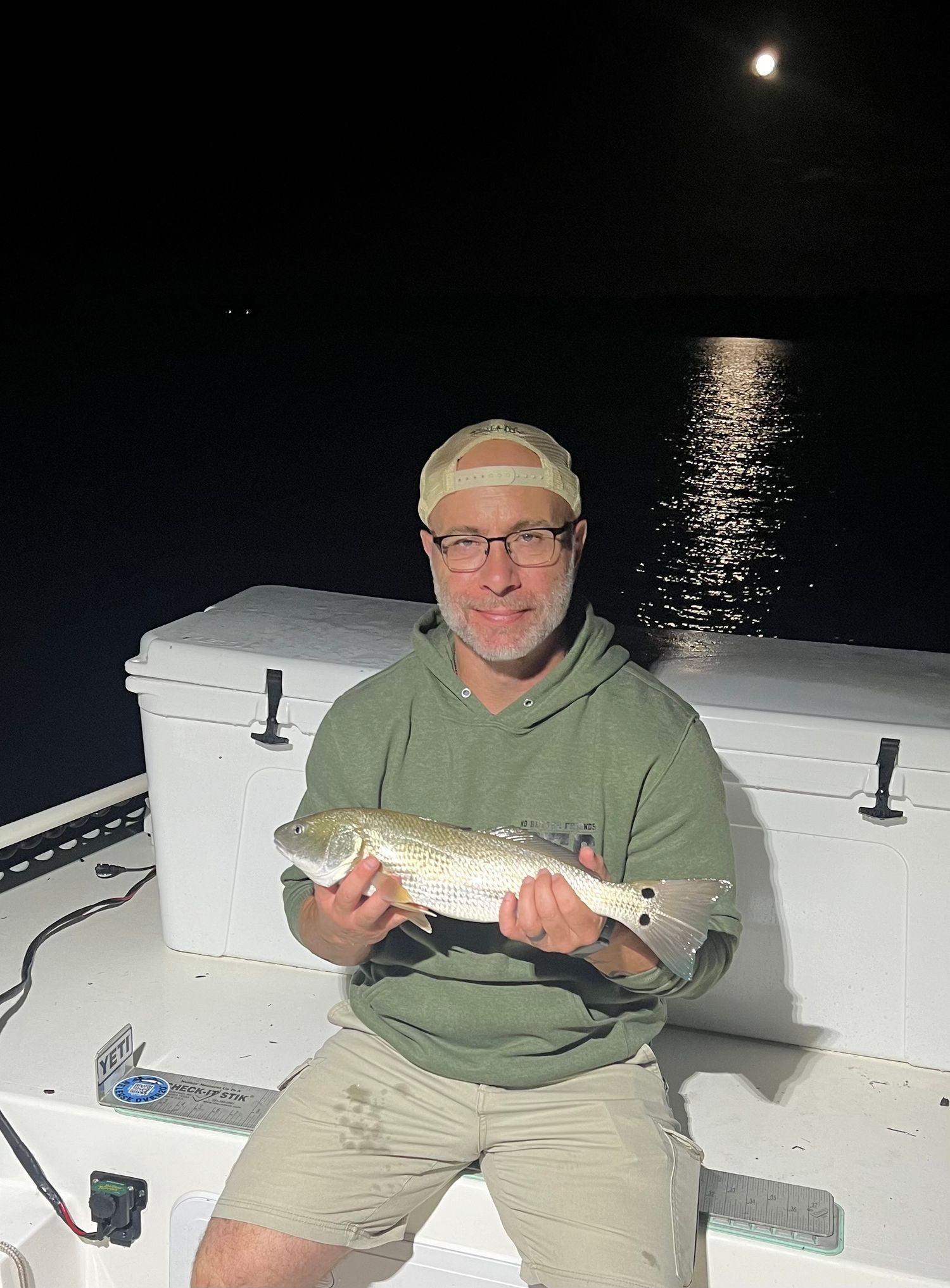 Moonlit fishing trip yielding nice-sized redfish catch near white cooler.