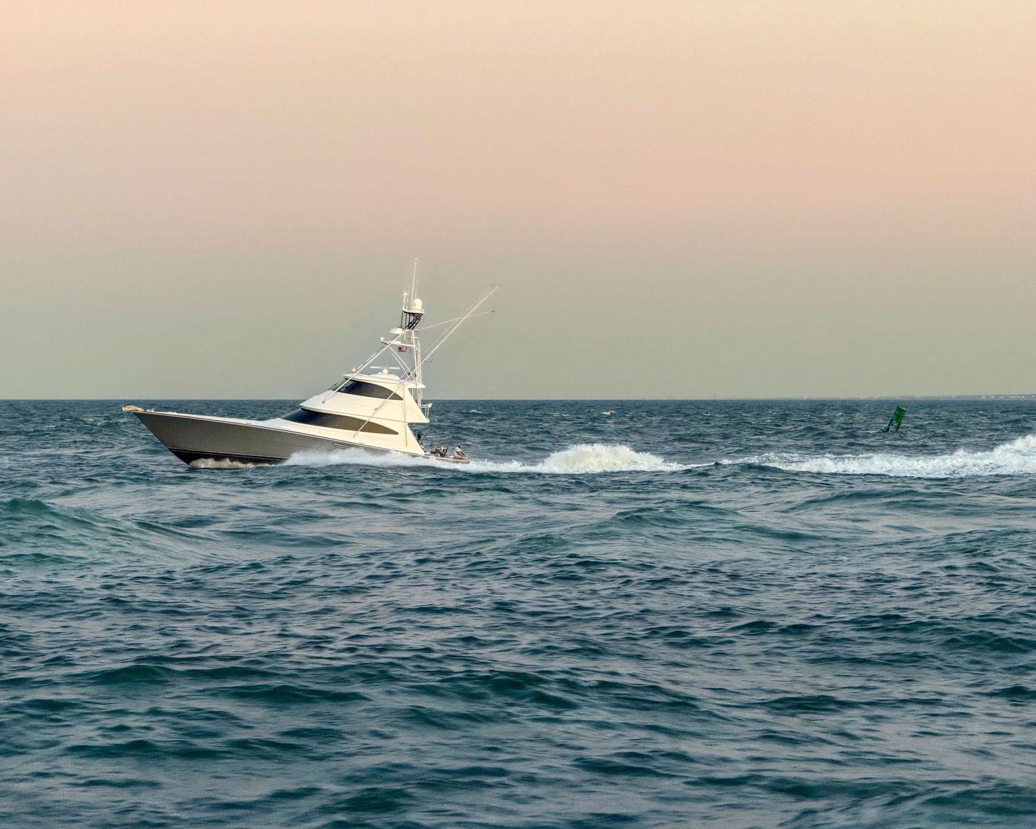 A white sport fishing yacht cruises through choppy ocean waters at dusk with a pastel sky on the horizon.