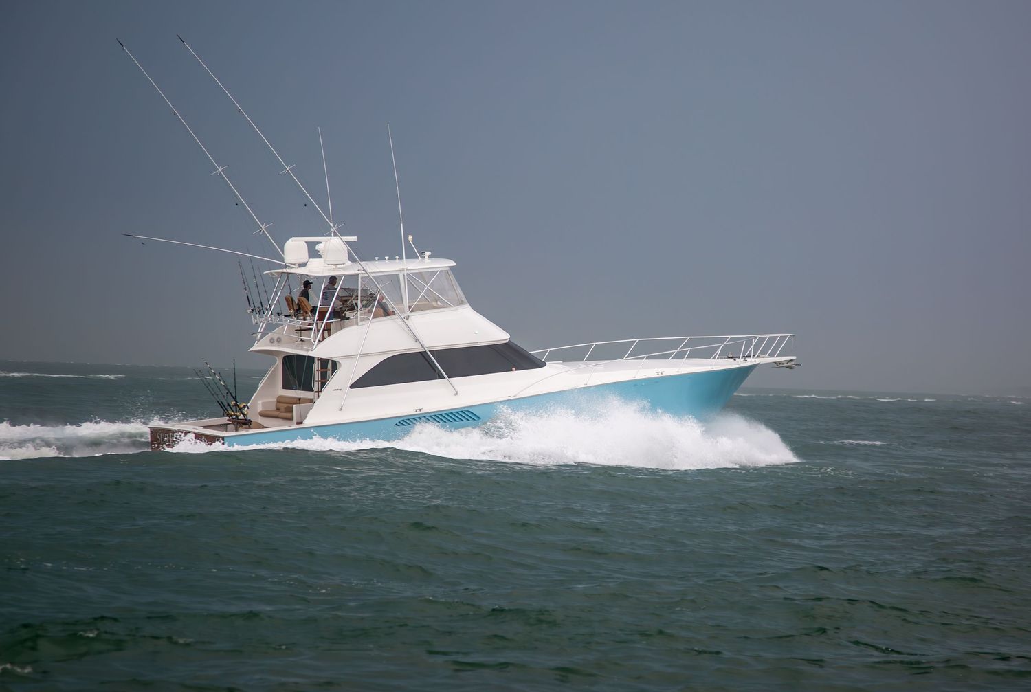 Large sport fishing yacht with blue trim cuts through rough ocean waters.