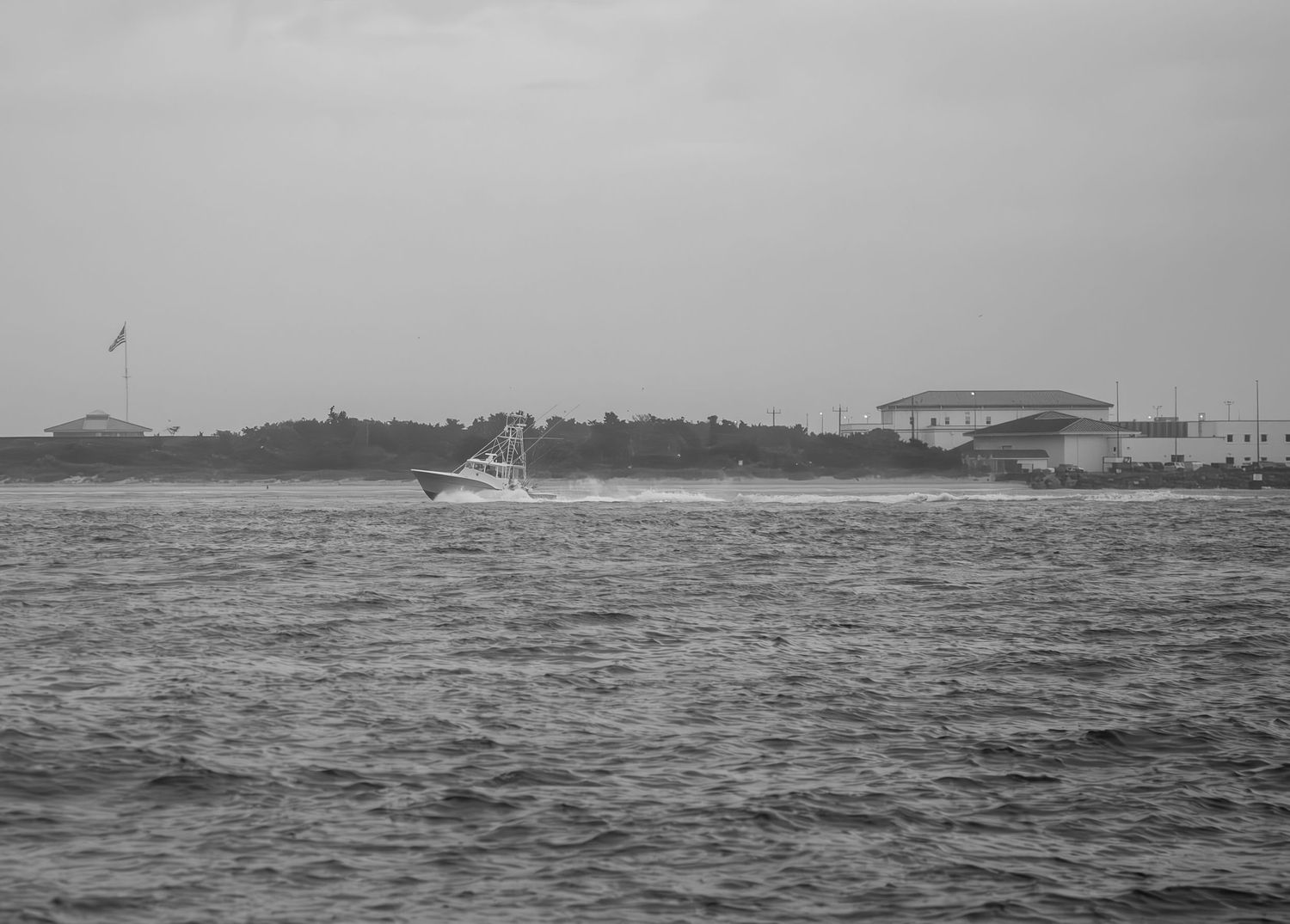 Black and white photo of a boat sailing across choppy waters with buildings visible on the shoreline.