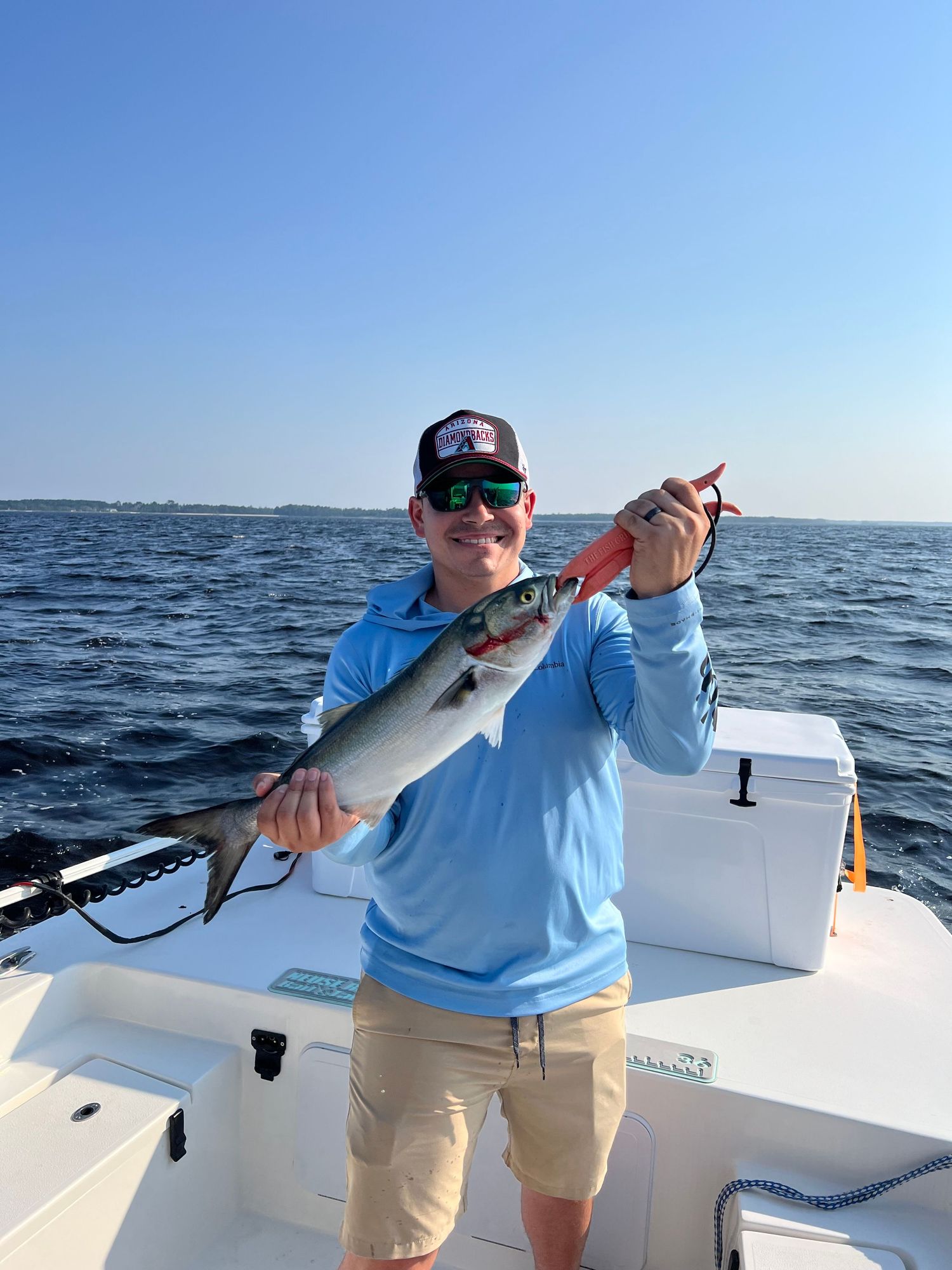 Angler displaying caught fish while standing on white boat deck with ocean backdrop.