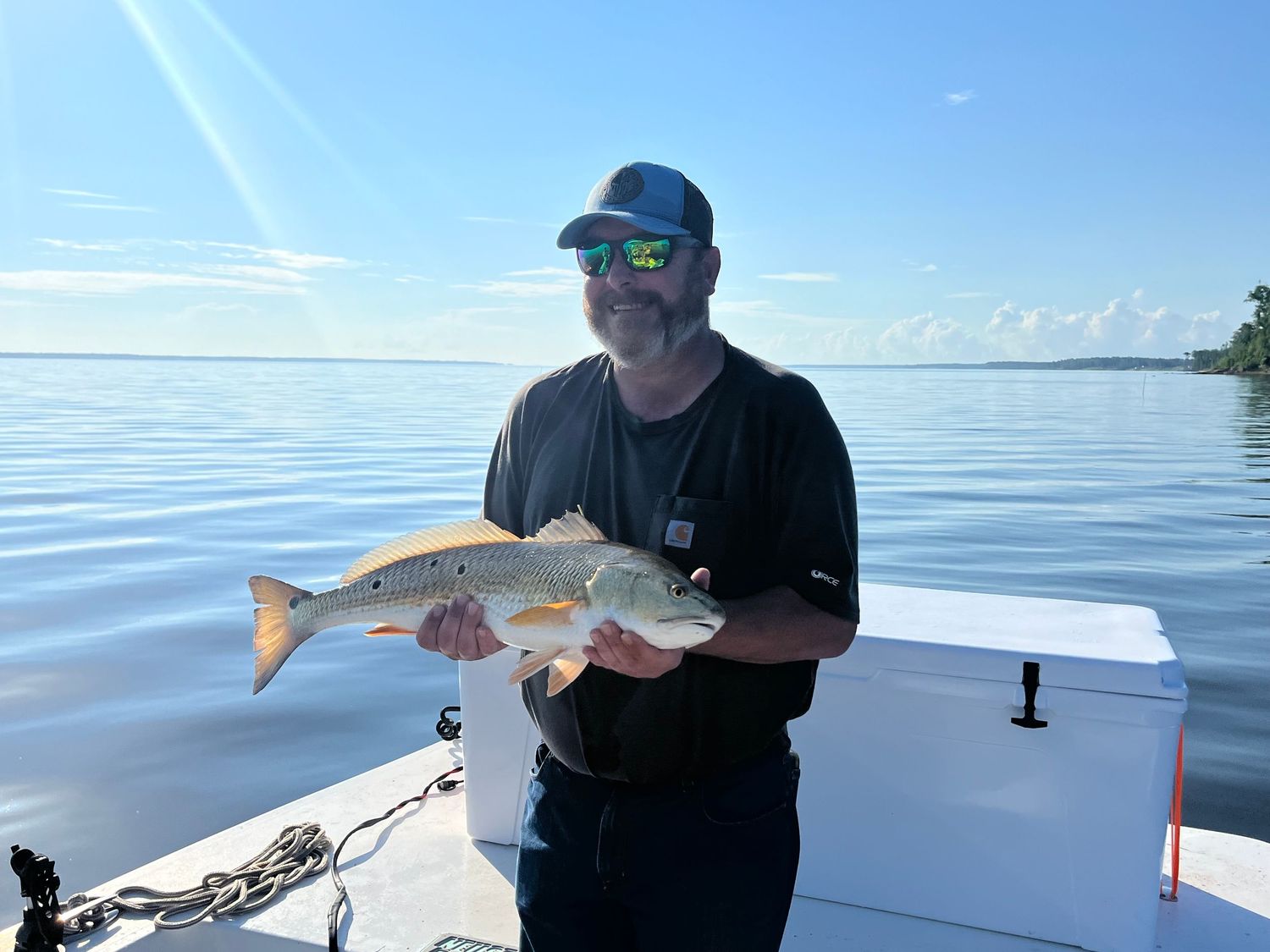 Redfish caught during bright sunny day on calm waters from white fishing boat.