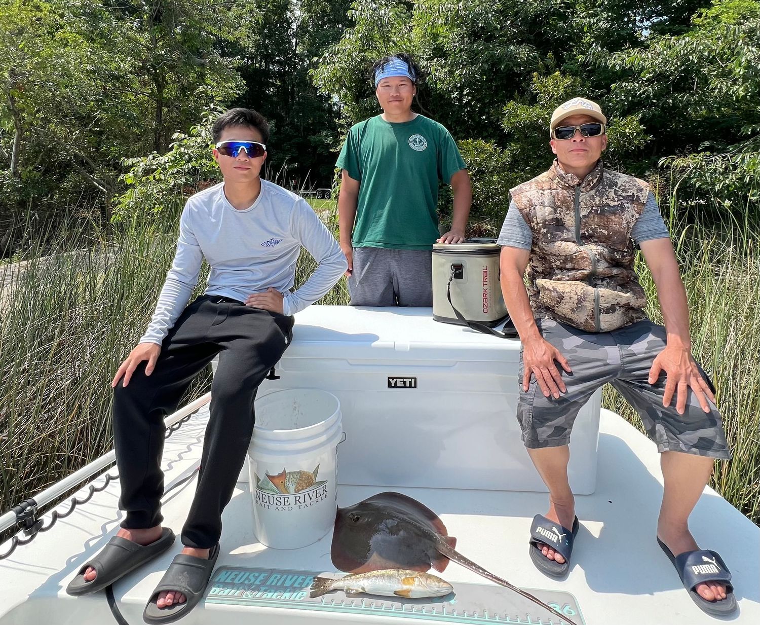 Group relaxing on fishing boat with catch near coastal marsh grass.
