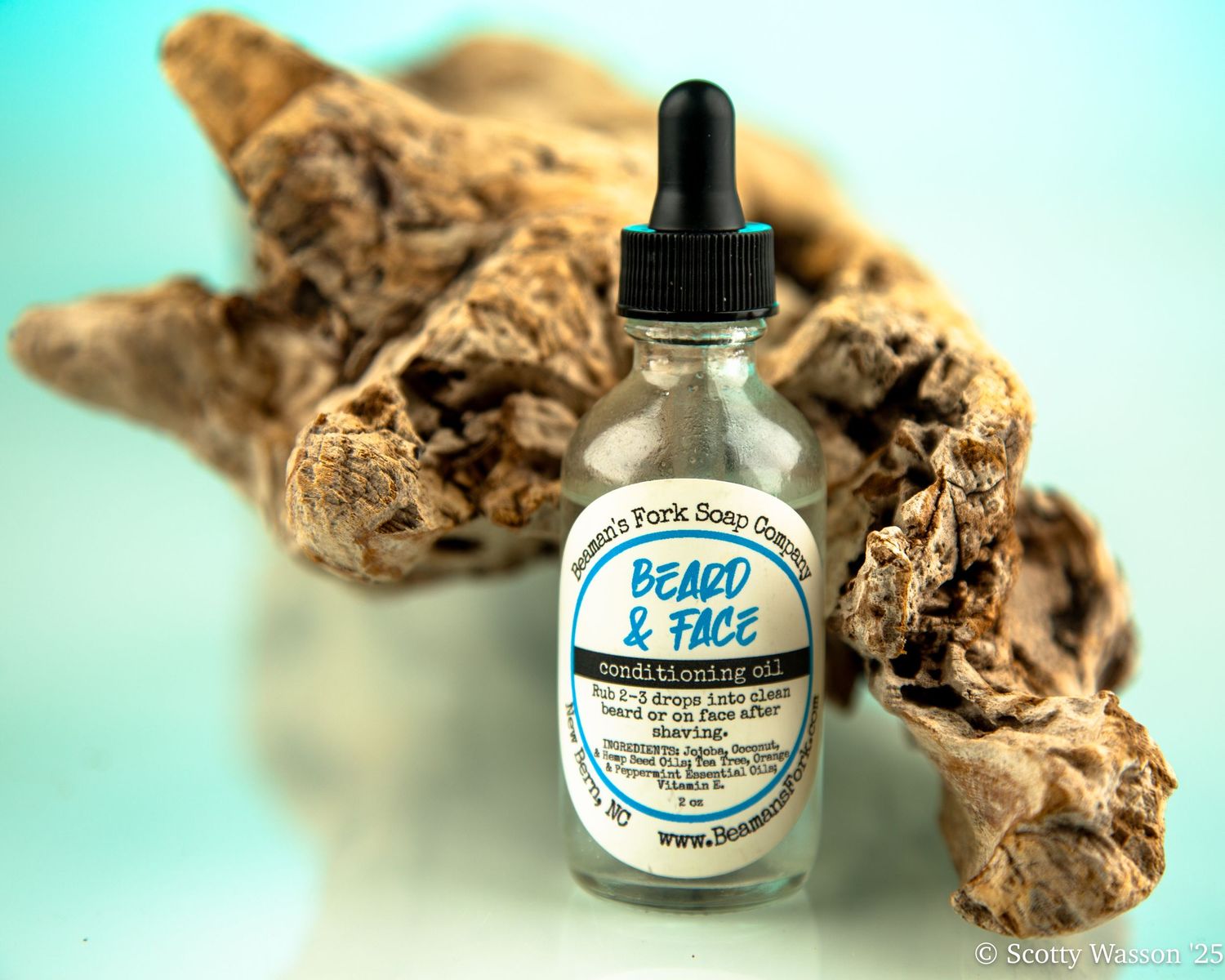 Beaver's Fork Soap beard and face conditioning oil bottle with dropper, displayed against driftwood on teal background.