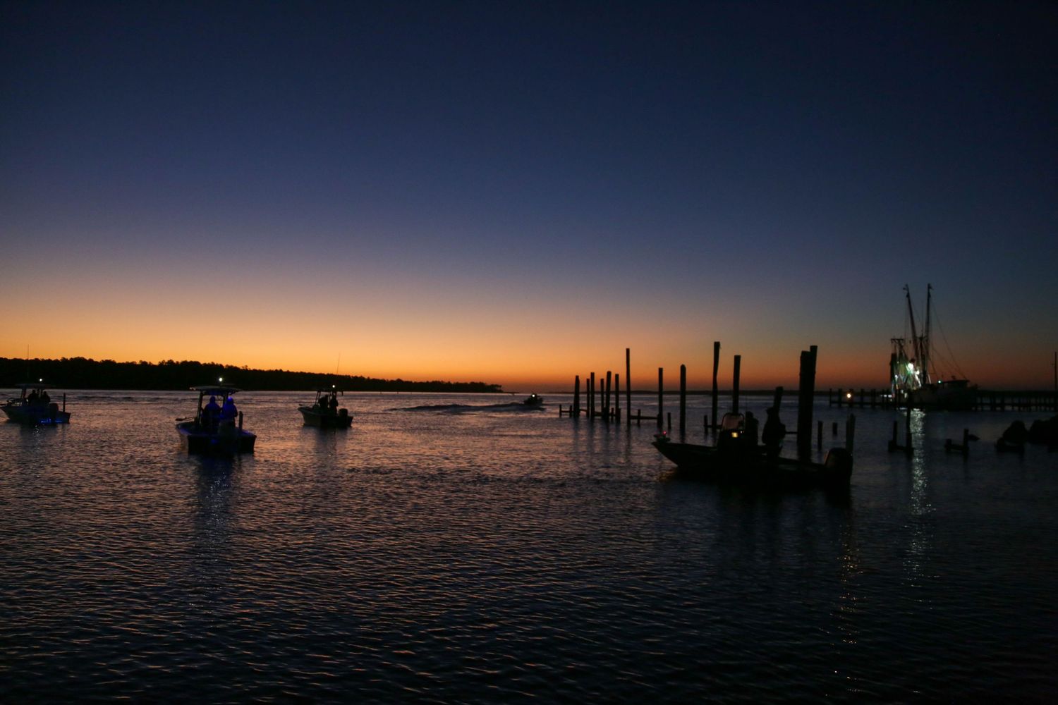 Silhouette of boats and dock posts during colorful sunset over water.
